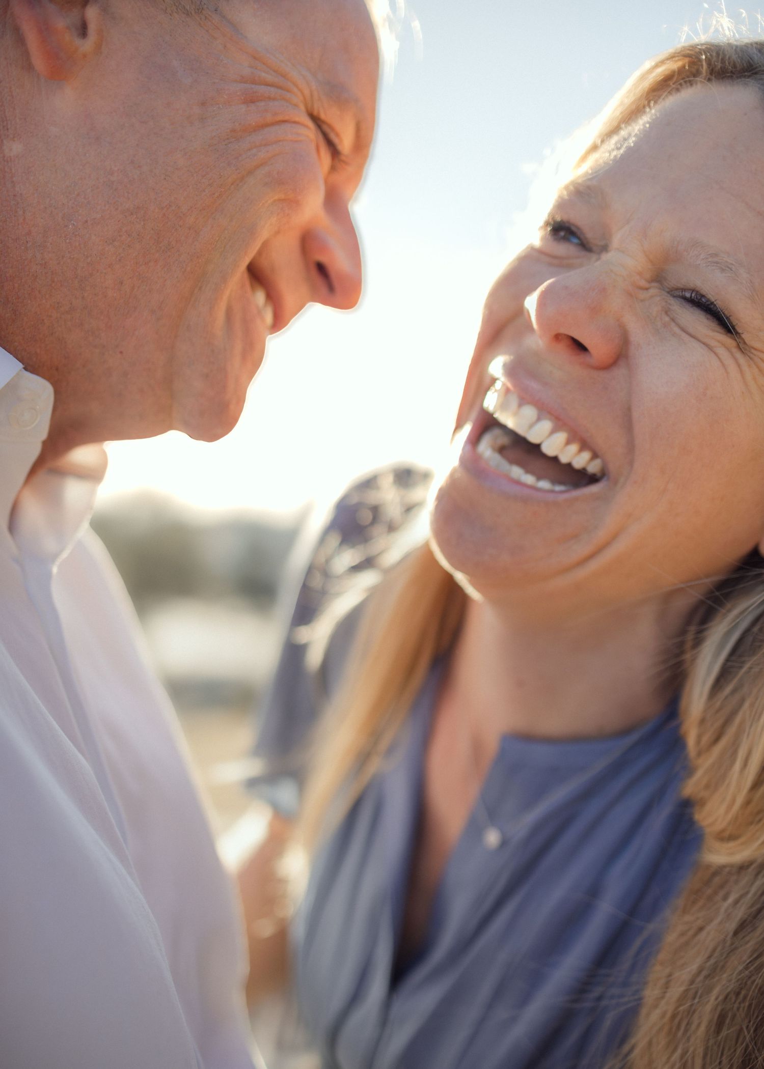 Middle-aged couple laughing and sharing a joyful moment outdoors in warm sunlight.