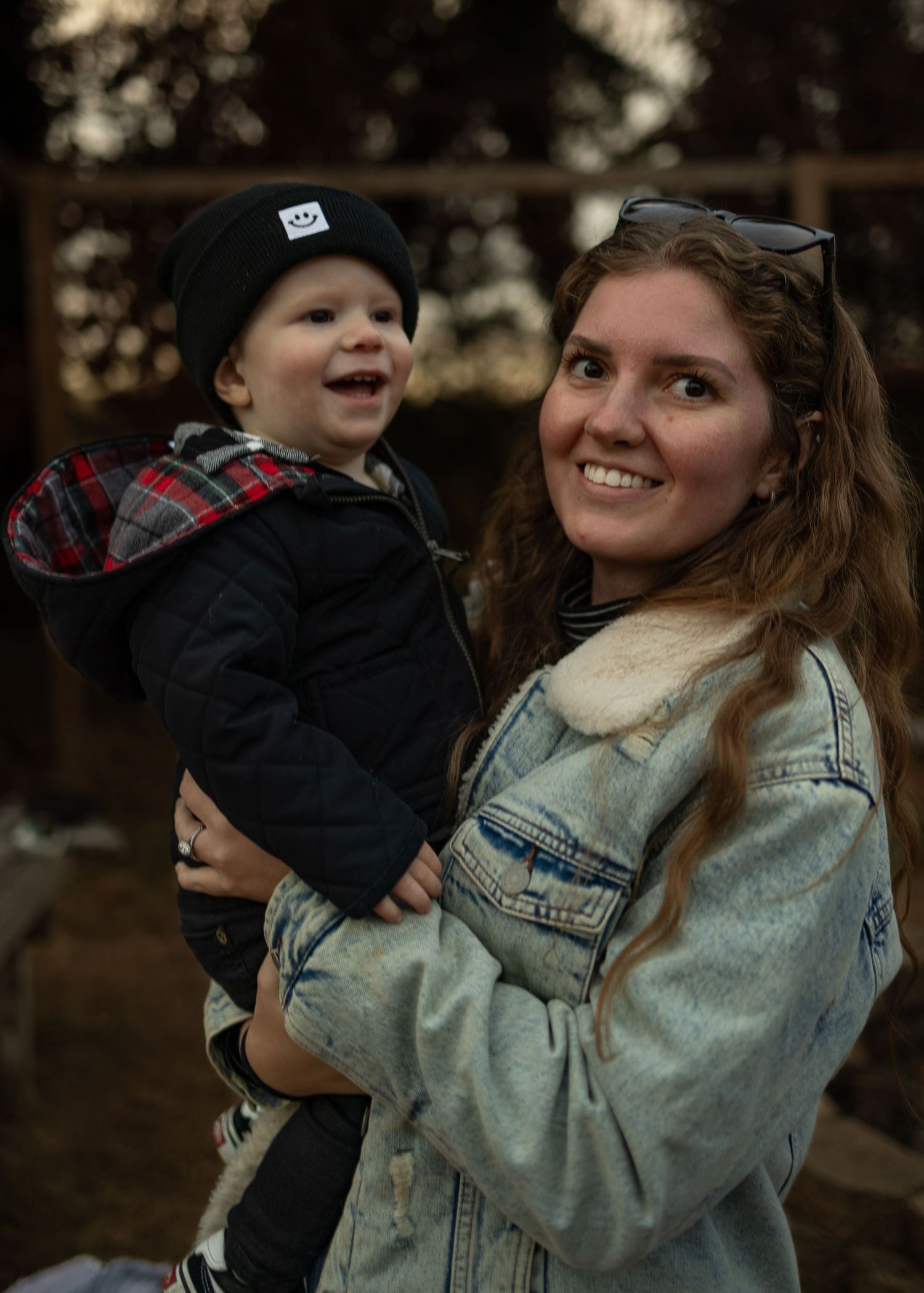 A parent and young child share a joyful moment outdoors wearing casual fall attire including denim and plaid.