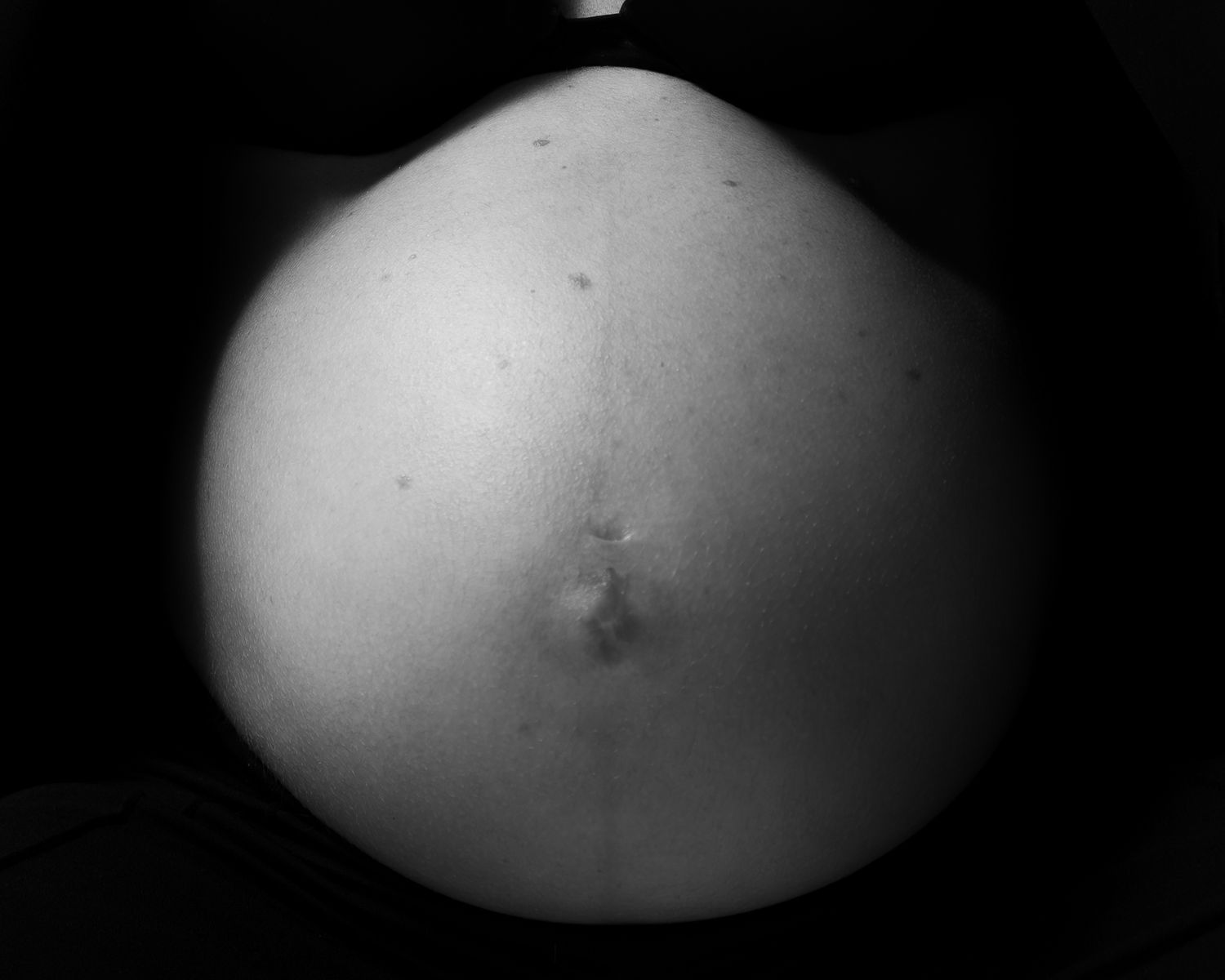 Black and white close-up photo of a pregnant woman's bare baby bump showing third trimester belly.