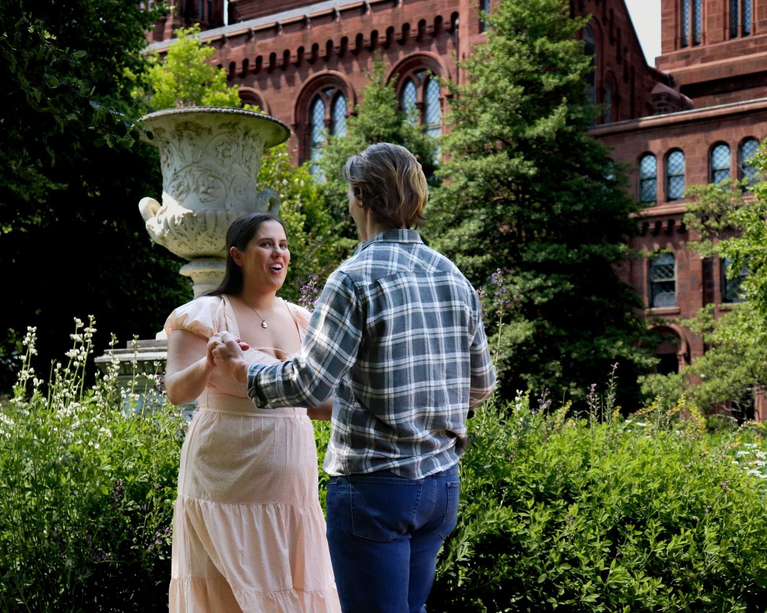 Engaged couple walking through garden near Smithsonian Castle red brick facade, Washington DC engagement photography.