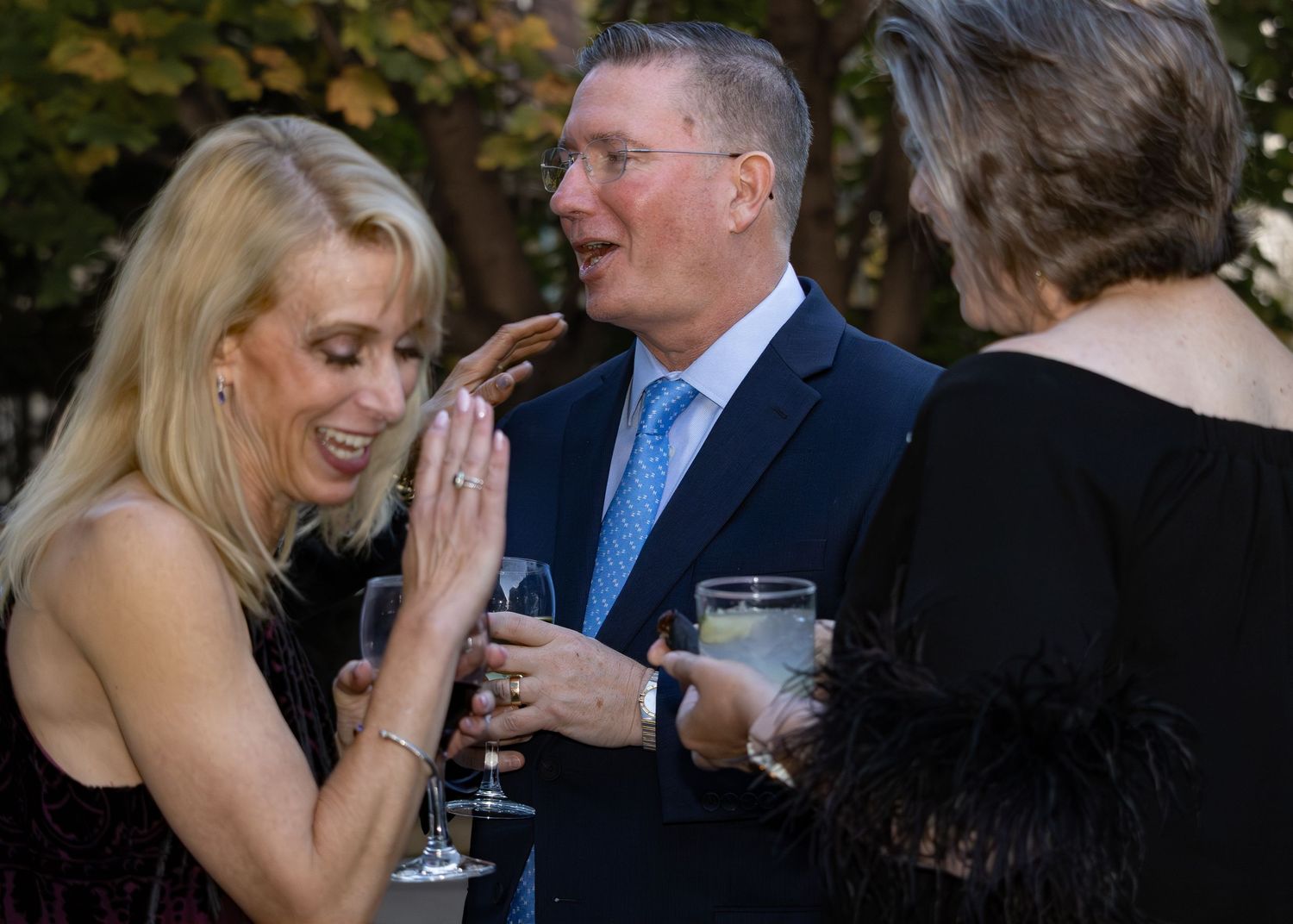Candid reception photos show joyful wedding guests laughing and socializing while holding wine glasses at an evening event.