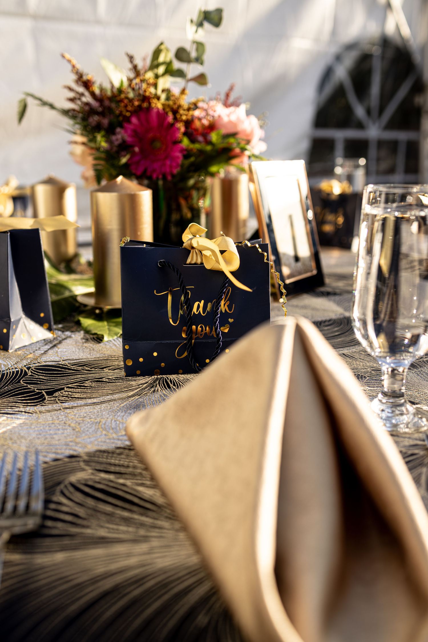 Elegant table settings with gold accents, navy blue place cards, and beige napkins in natural lighting.