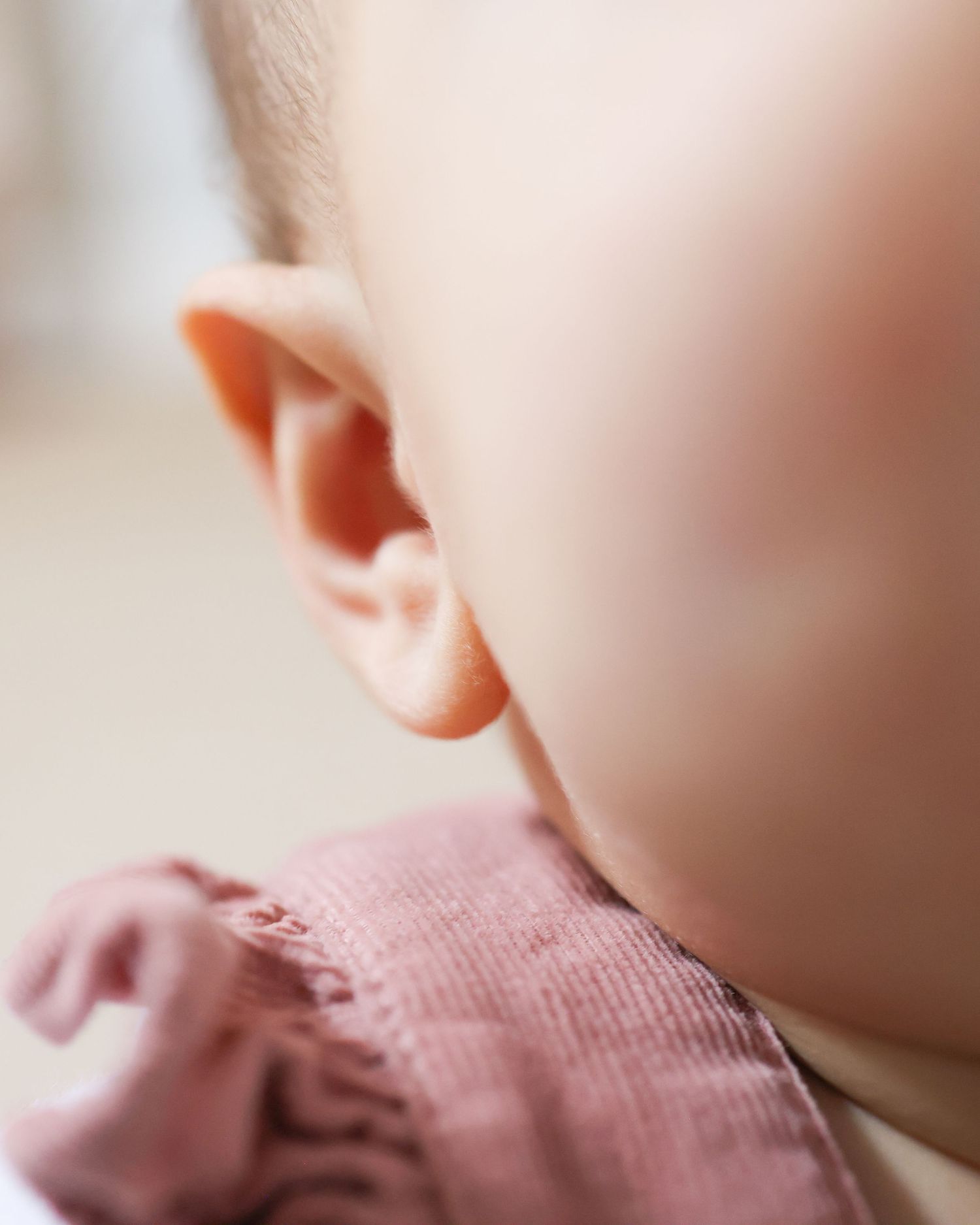 Close-up view of a baby's ear and cheek showing soft delicate skin in gentle lighting.