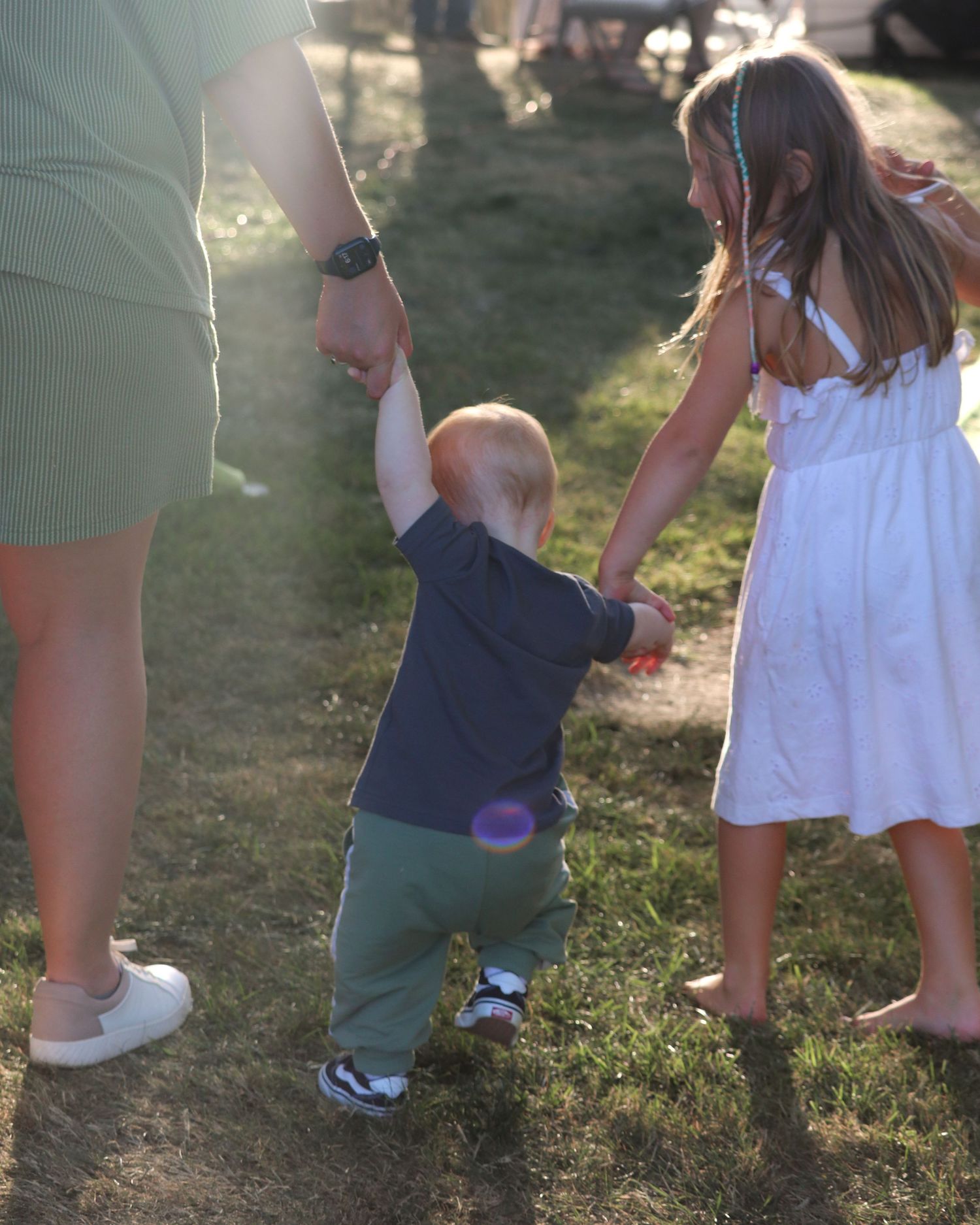 Close-up view of legs and feet of people walking on grass during an outdoor gathering.