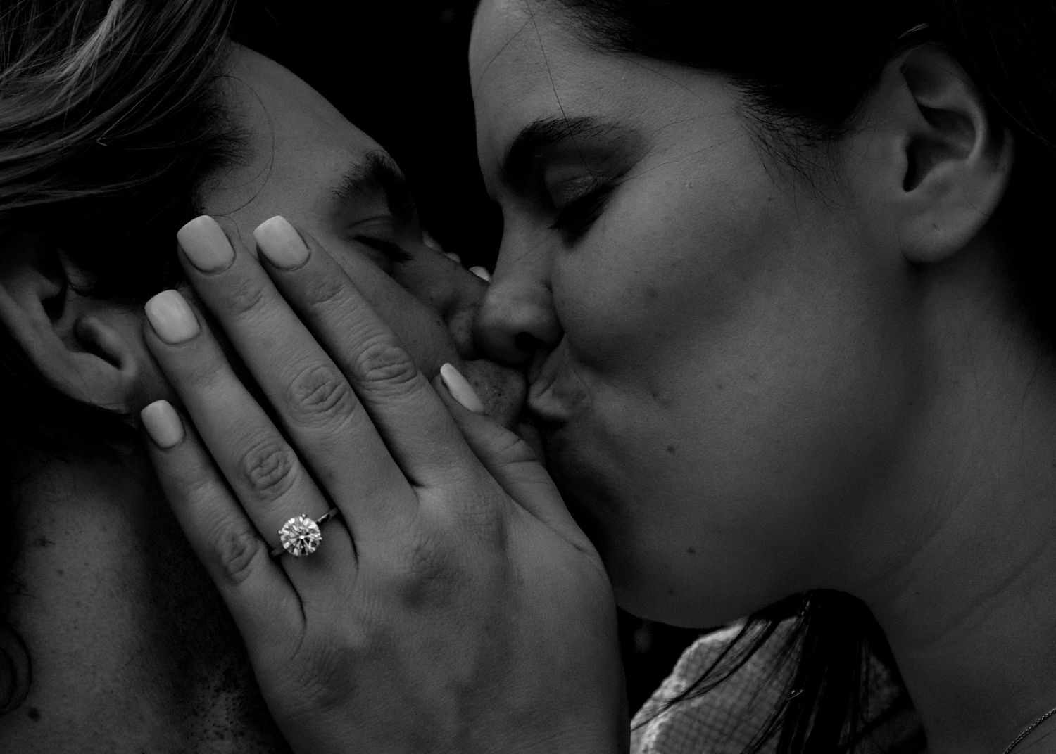 A romantic black and white engagement photo showing a close up kiss and sparkling diamond ring.