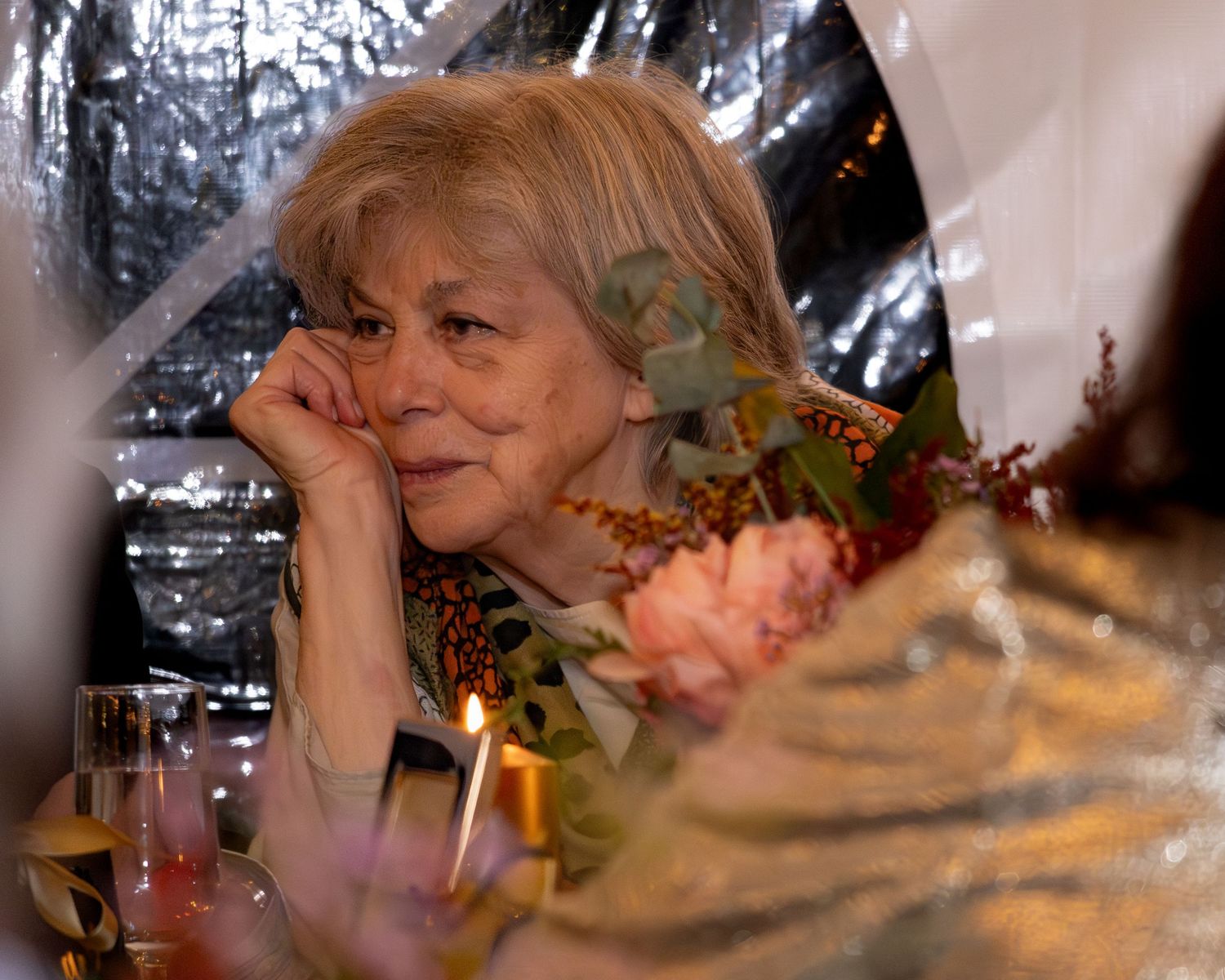 A person blows out birthday candles on a cake in a dimly lit room with festive decorations.
