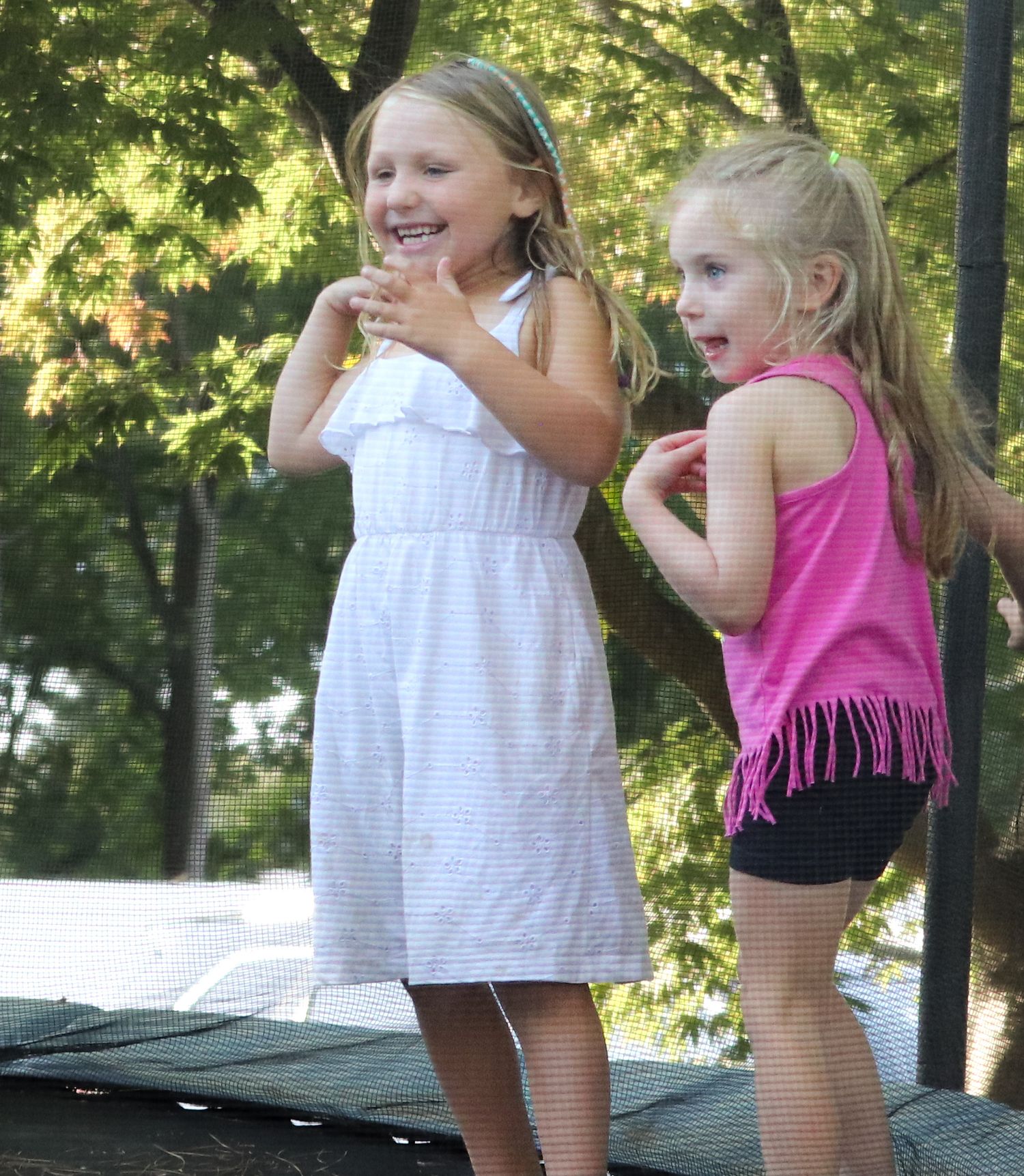 Two girls laugh and play together on outdoor furniture on a sunny summer day.