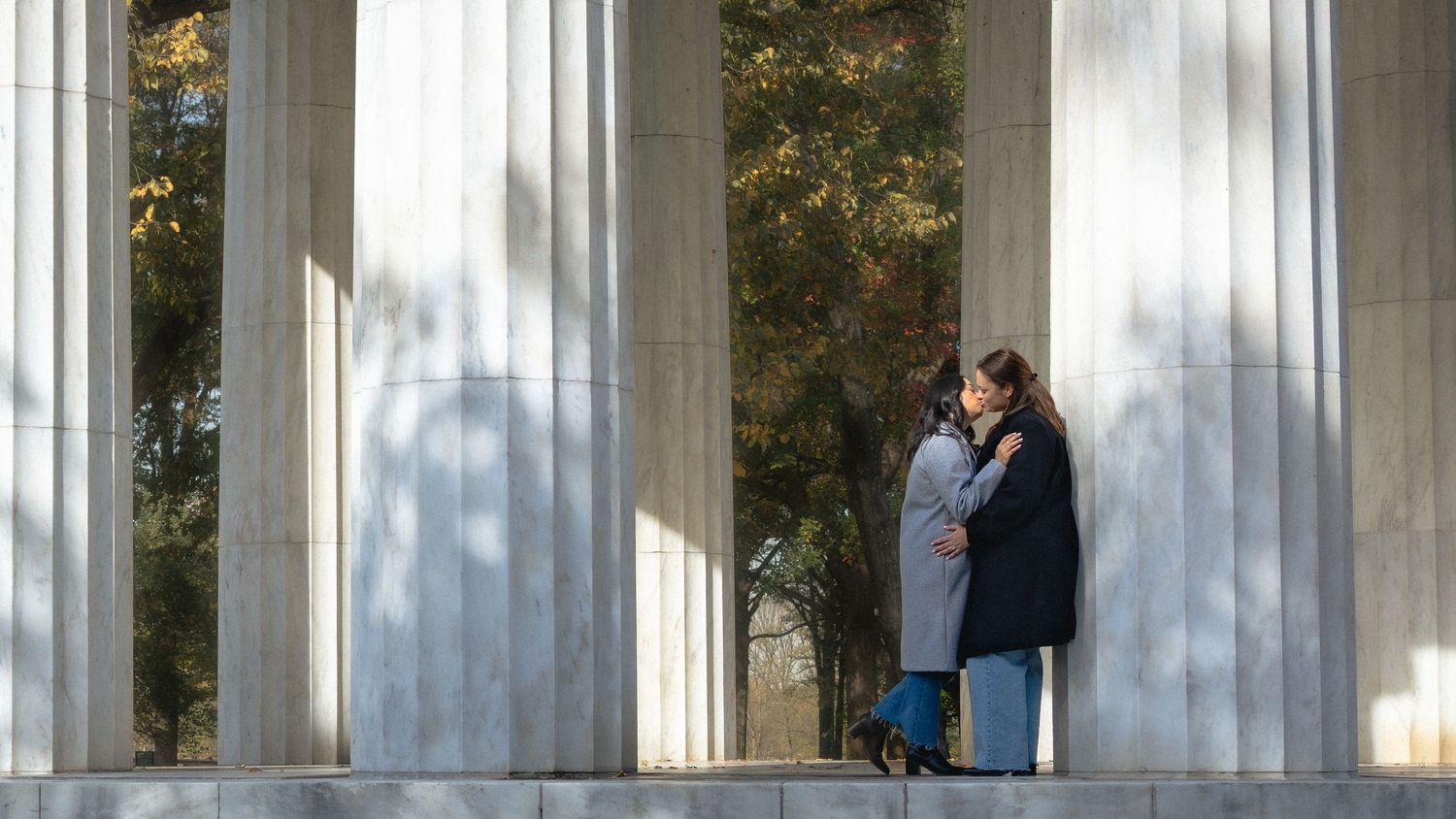 Lesbians embrace between tall white marble columns at the War Memorial in Washington D.C.