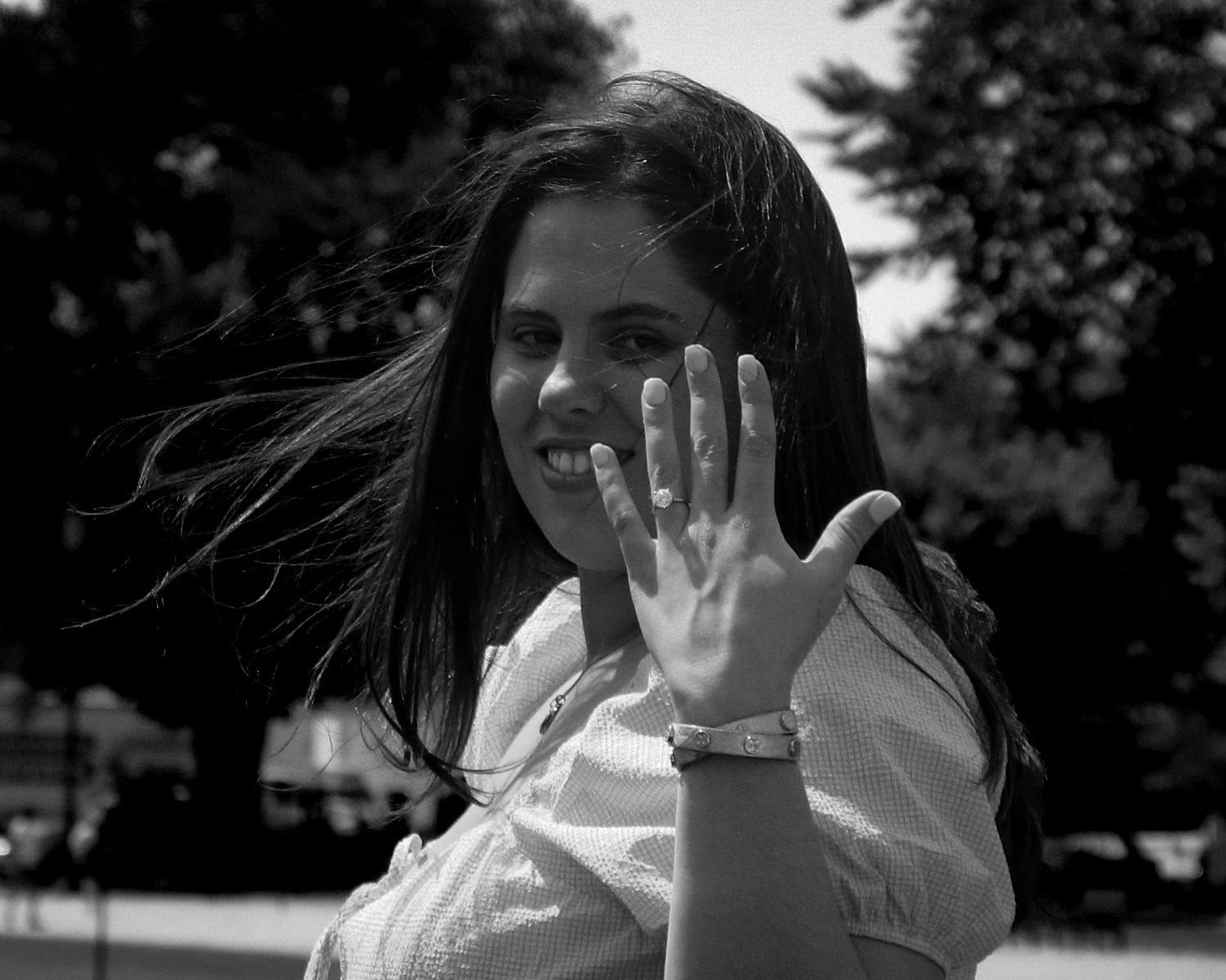 Black and white engagement portrait of woman smiling and waving her ring, candid moment during DC couple session.