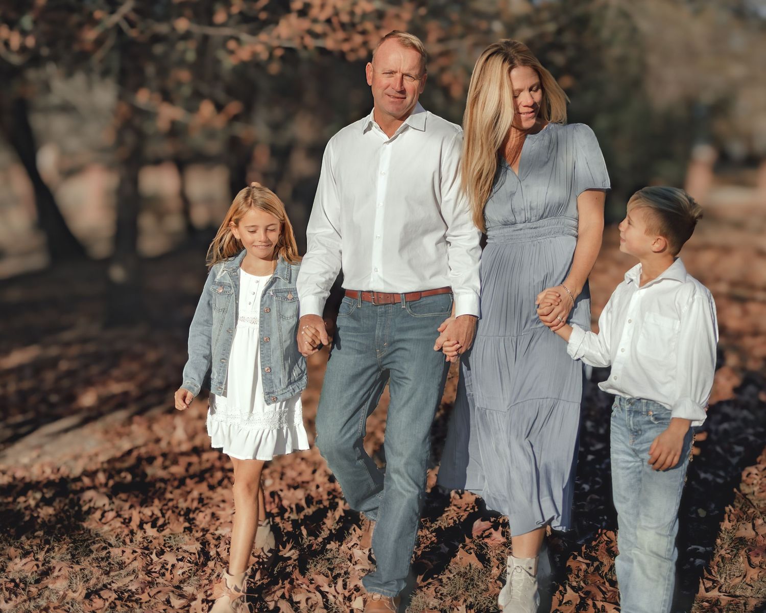 Family of four walking outdoors in coordinated blue and white outfits among autumn trees.