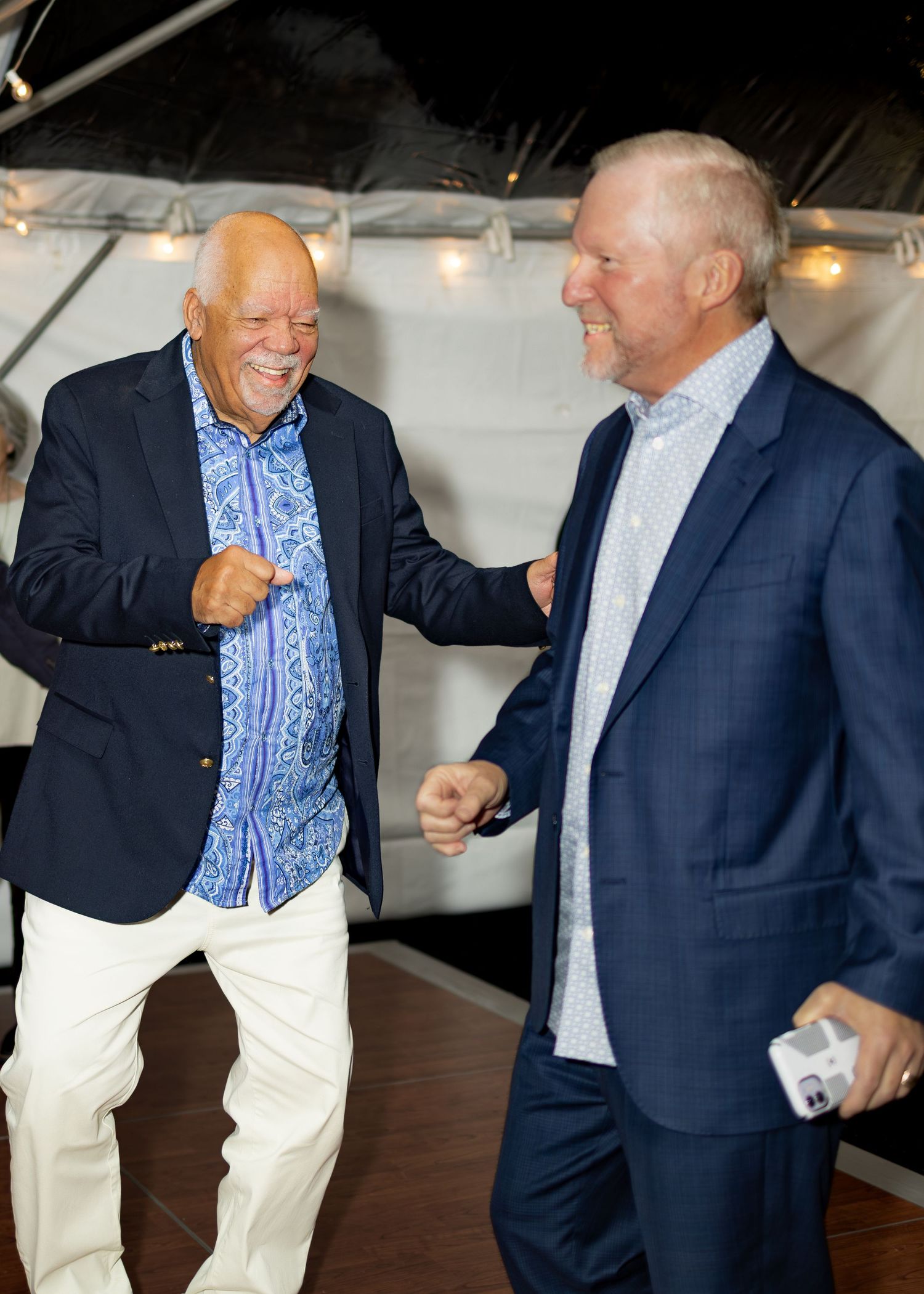 Two men in contrasting outfits engage in animated conversation in a casual indoor setting.