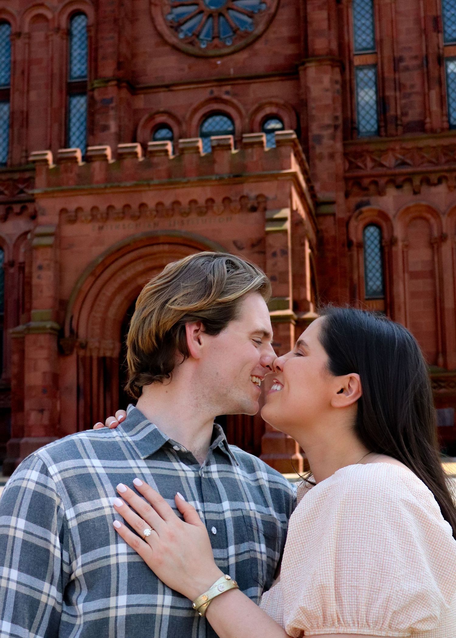 An engaged couple shares a tender moment in front of the historic Smithsonian Castle with its ornate red brick architecture.