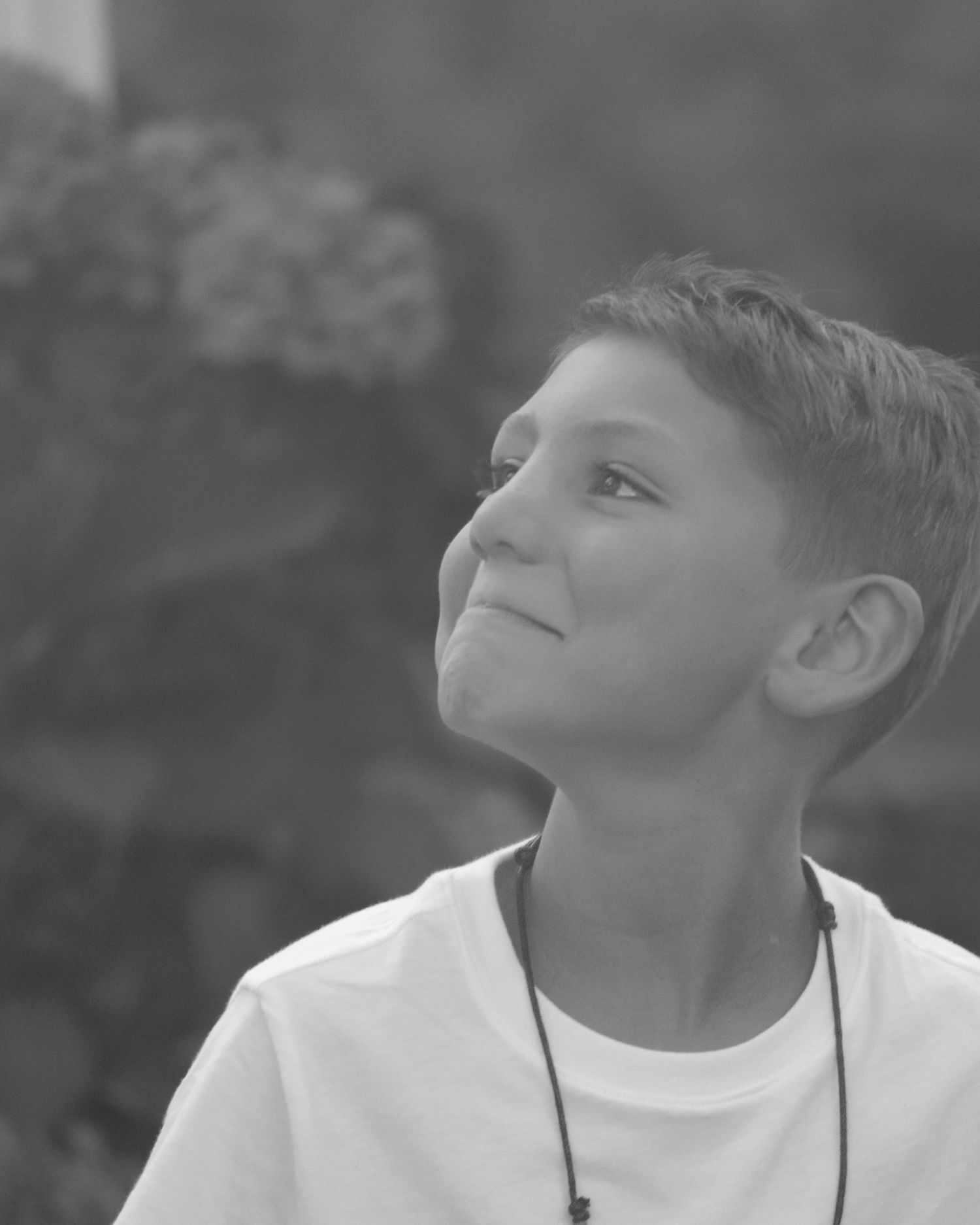 Young boy in white t-shirt looking up with expression of wonderment and curiosity in black and white photo series.