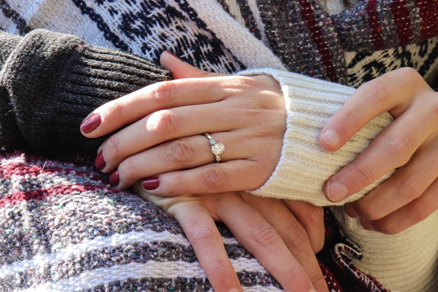 Close-up of hands wearing an engagement ring and cozy sweaters, symbolizing a romantic proposal moment.