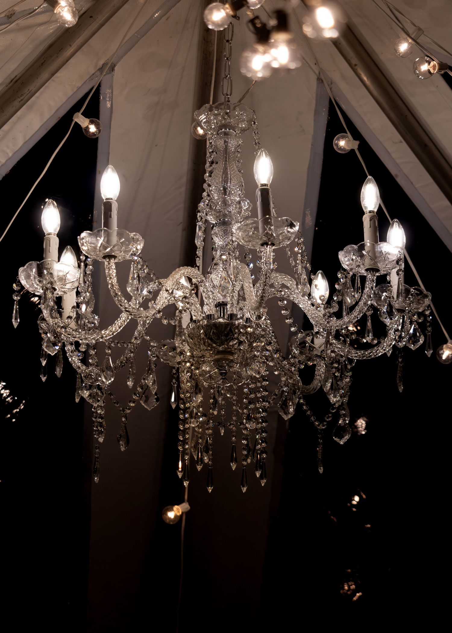 Elegant crystal chandeliers hanging from a draped ceiling create a romantic ambiance at an event venue.
