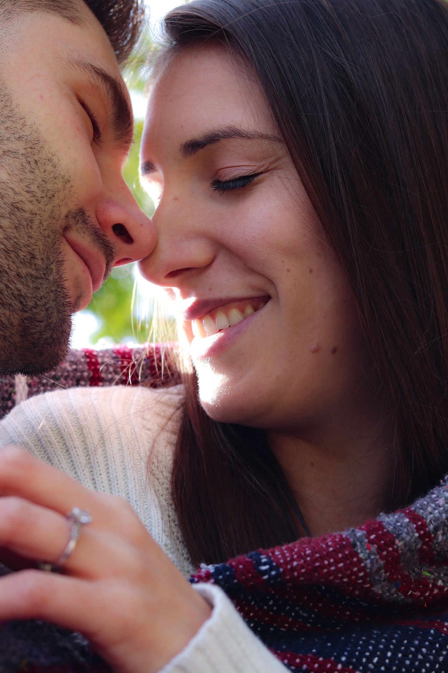 Romantic couple sharing a tender moment, smiling woman with ring and bearded man almost kissing outdoors.