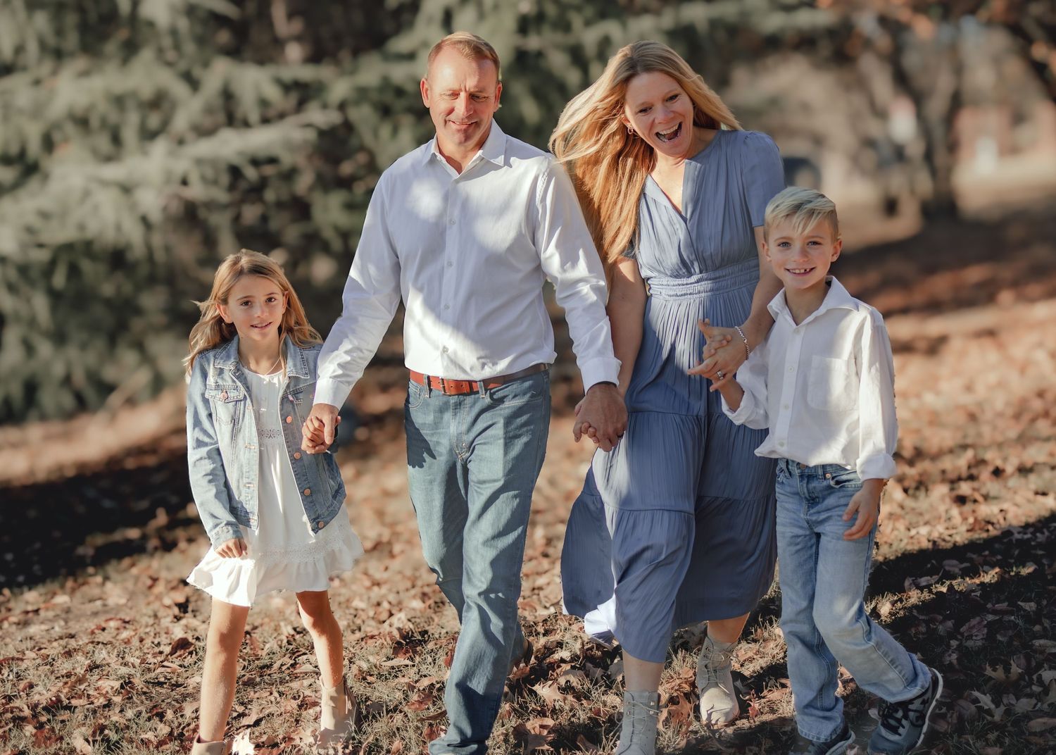 Happy family of four walking outdoors in coordinated blue and white outfits among autumn trees.