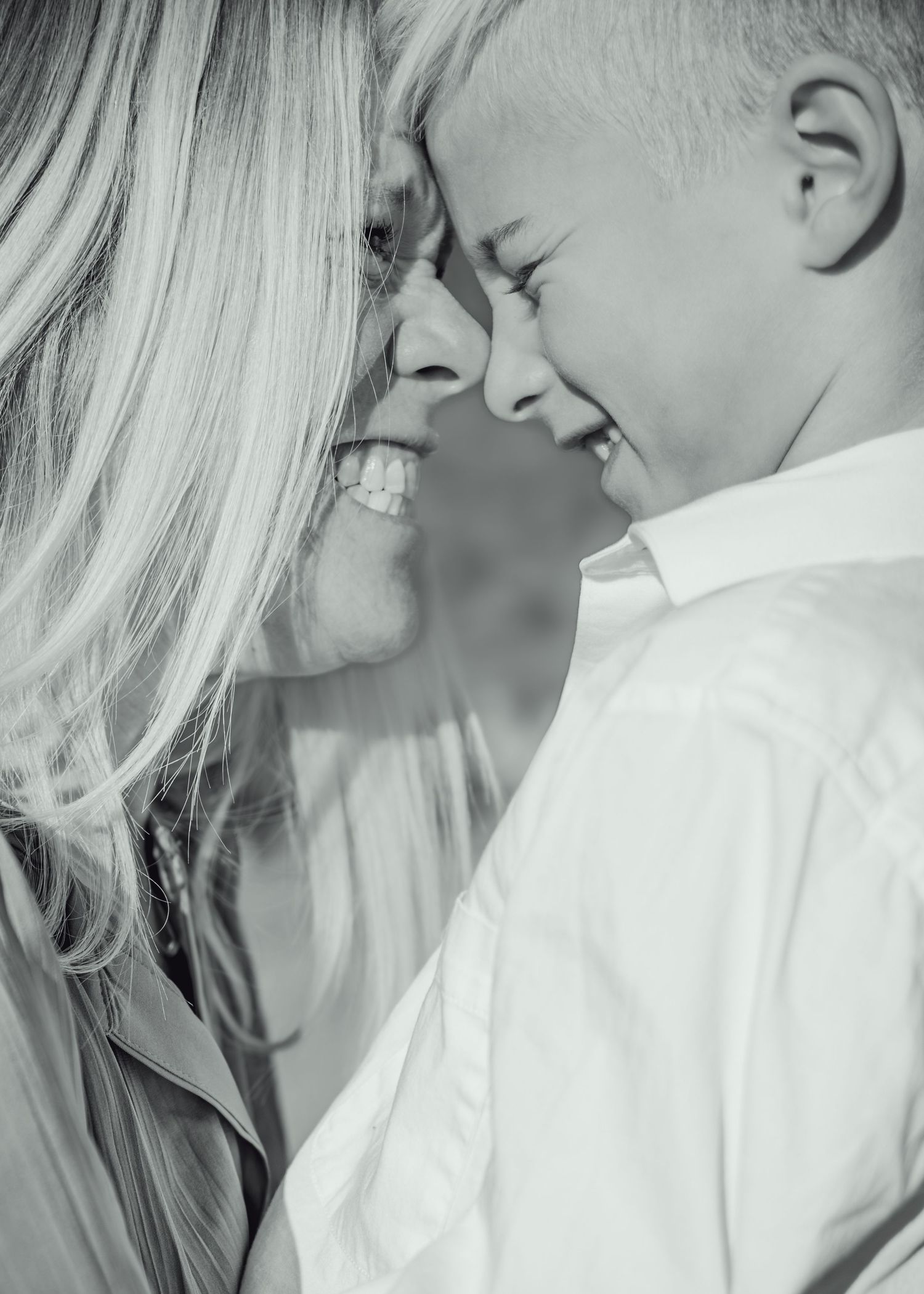 Black and white photo of a smiling woman and young boy touching foreheads in a tender, joyful moment.