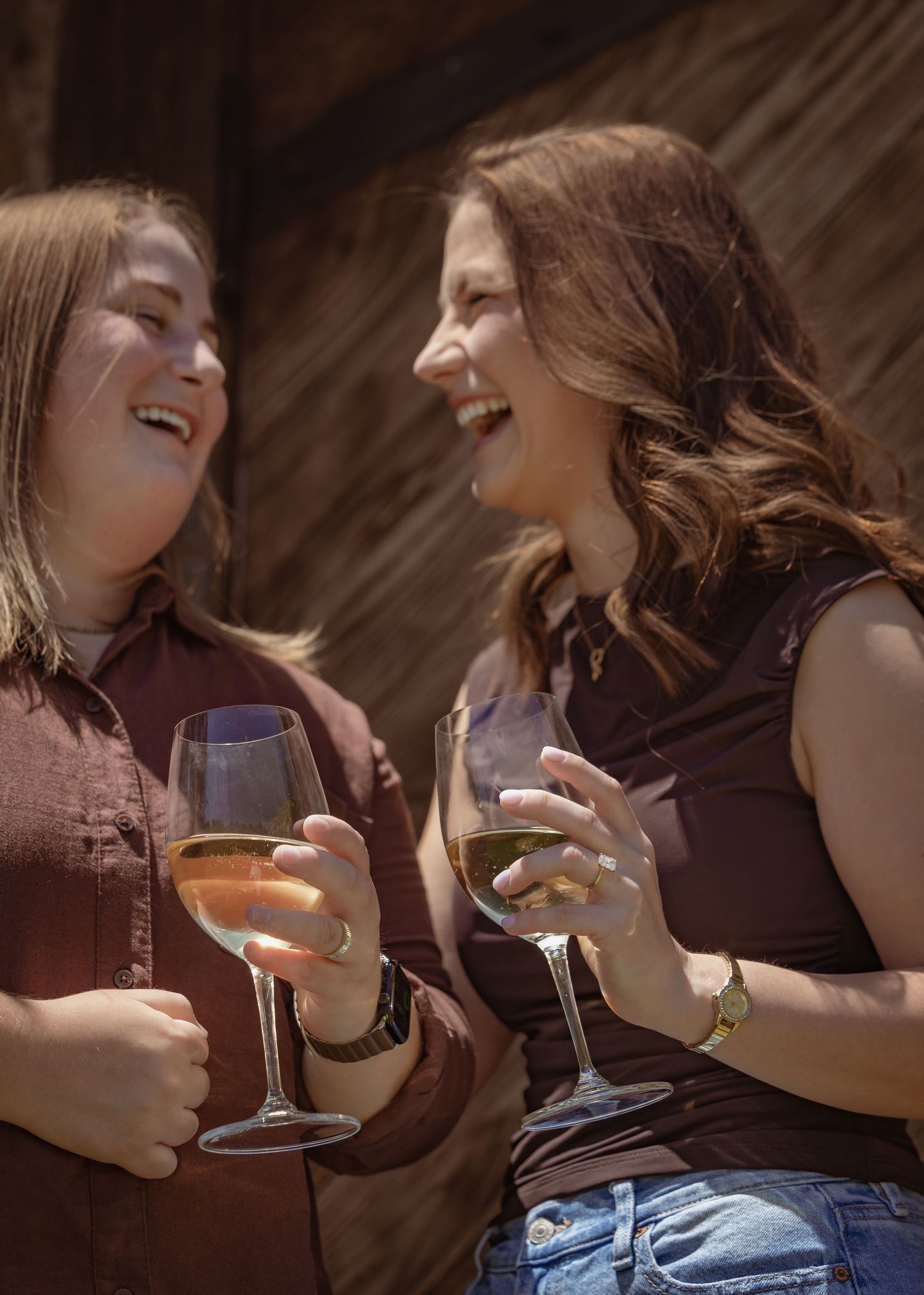 Two women laughing and enjoying wine glasses outdoors in warm sunlight, sharing a joyful moment together.