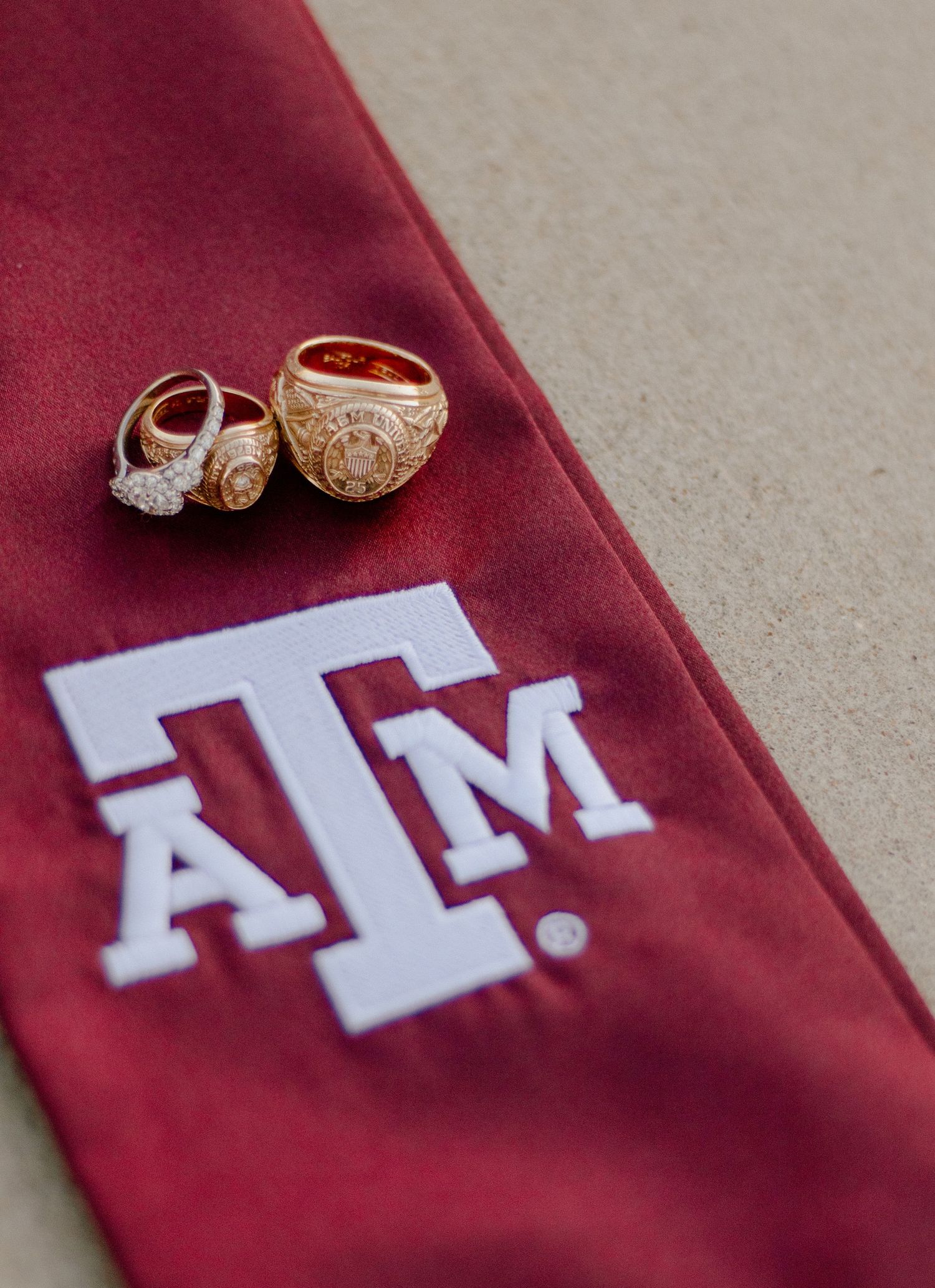 Maroon sash with Texas A&M logo and class rings displayed on textured surface.