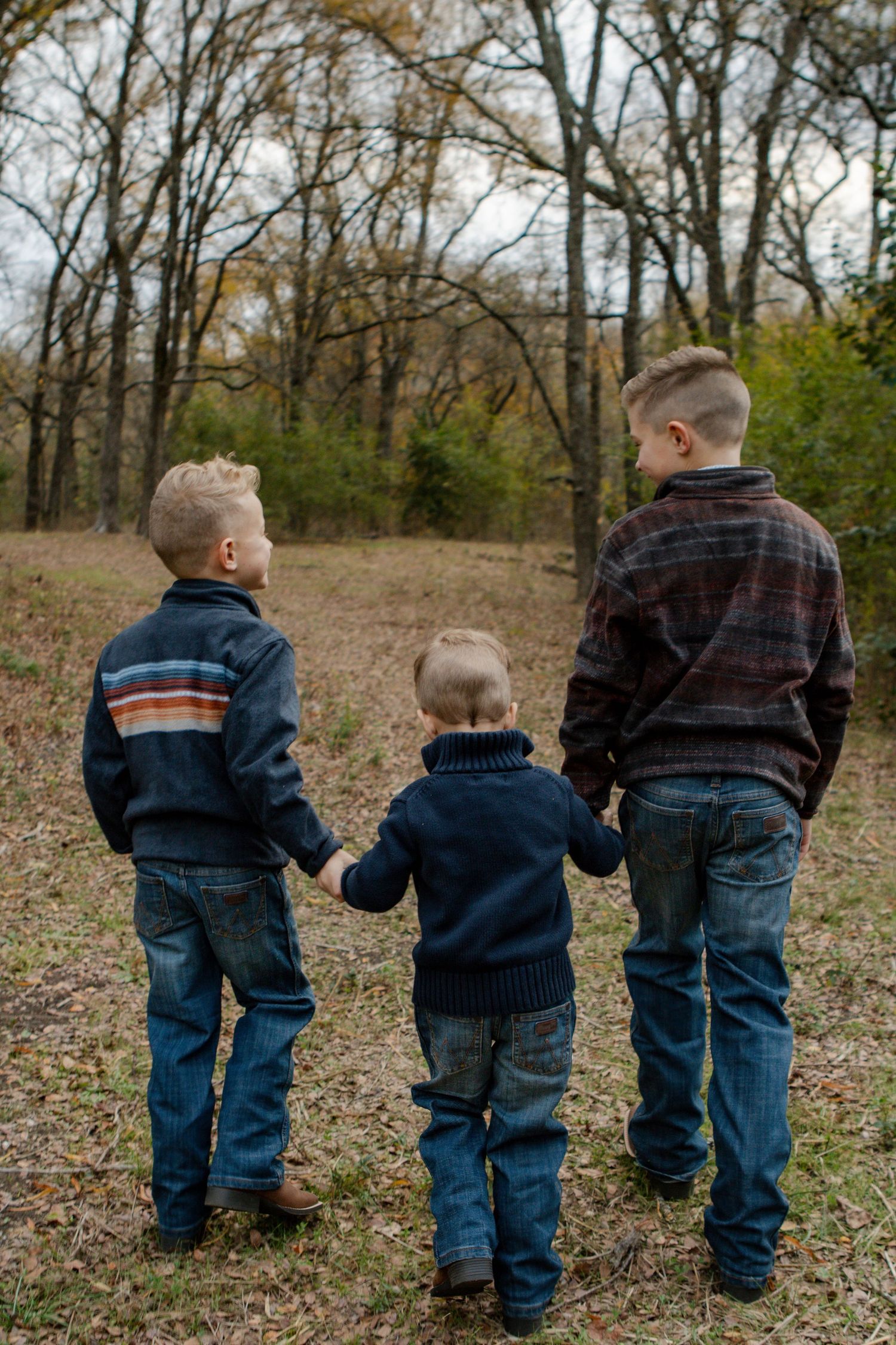 Three young children in matching denim and dark jackets stand together looking at nature.