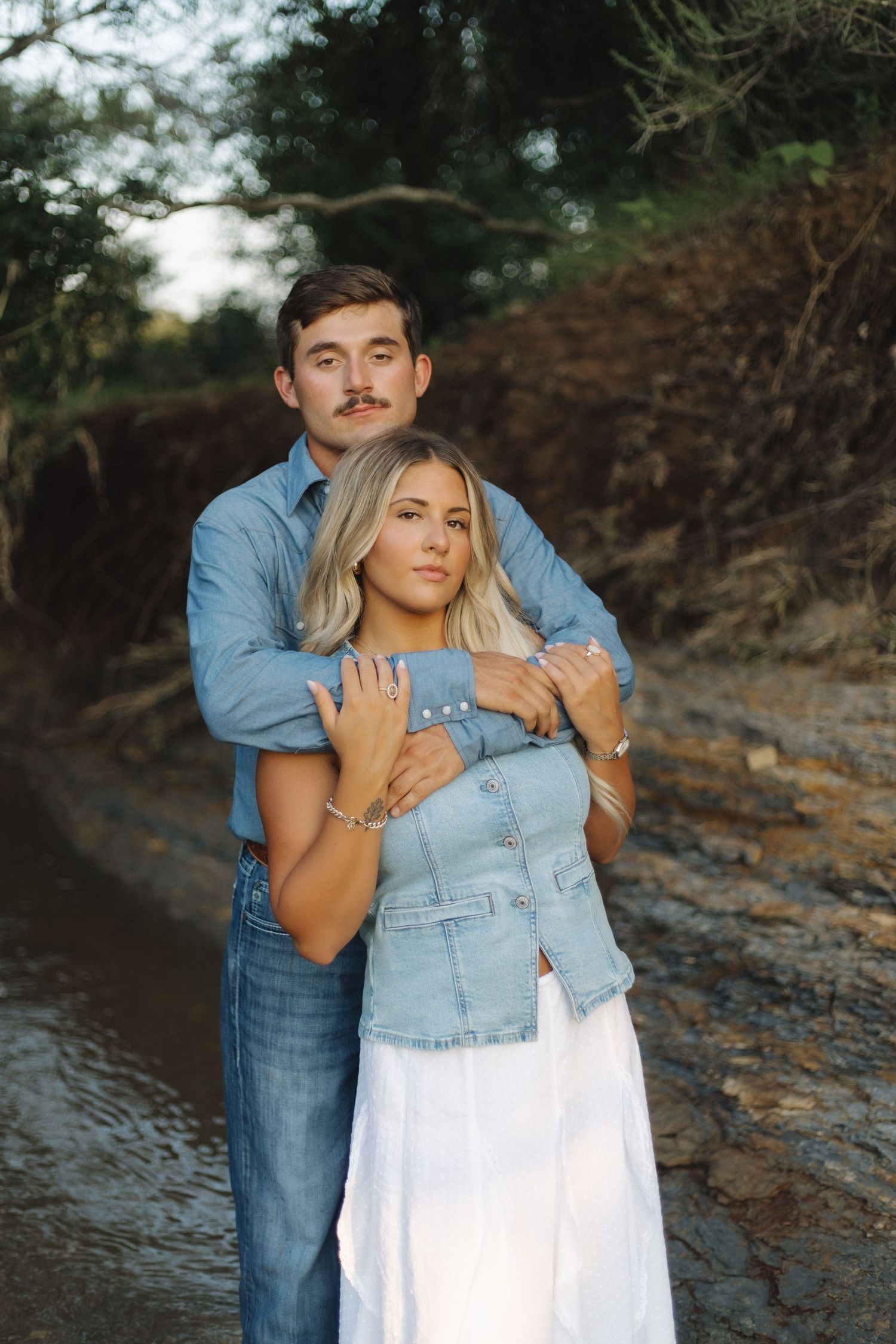Couple in denim and white embracing by rocky waterfront.