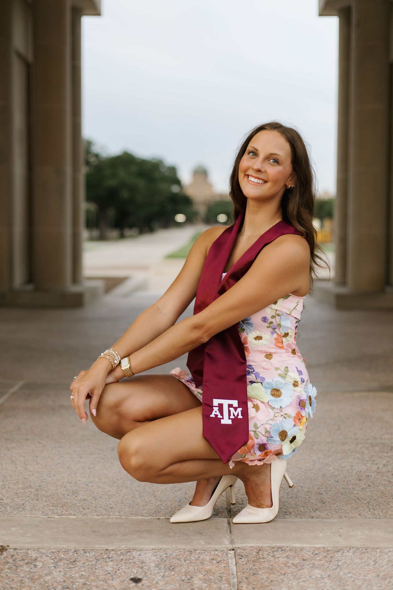 Graduate in floral dress and maroon stole poses near columns of university building.