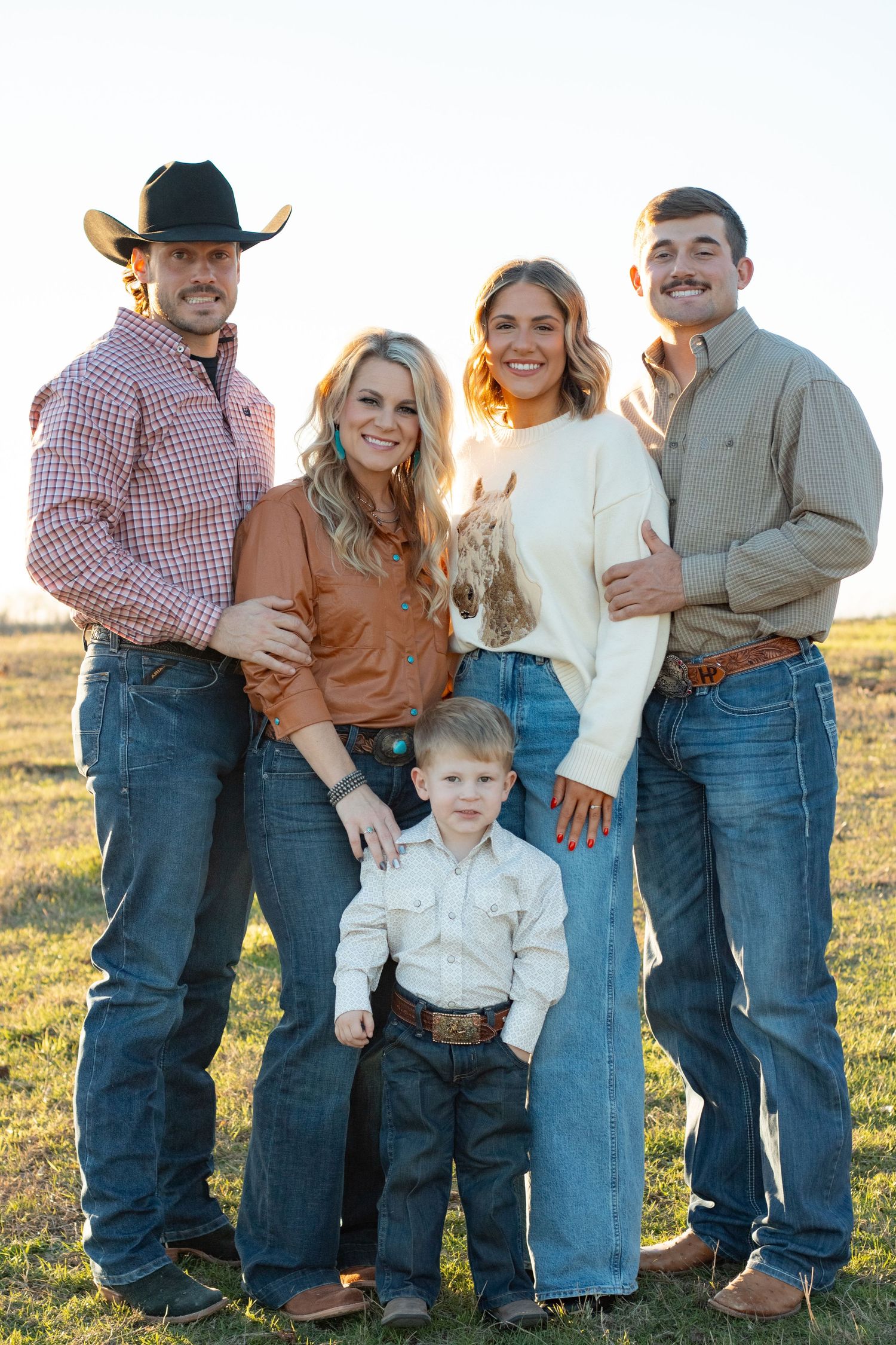 Extended family in western wear poses together in field at sunset.