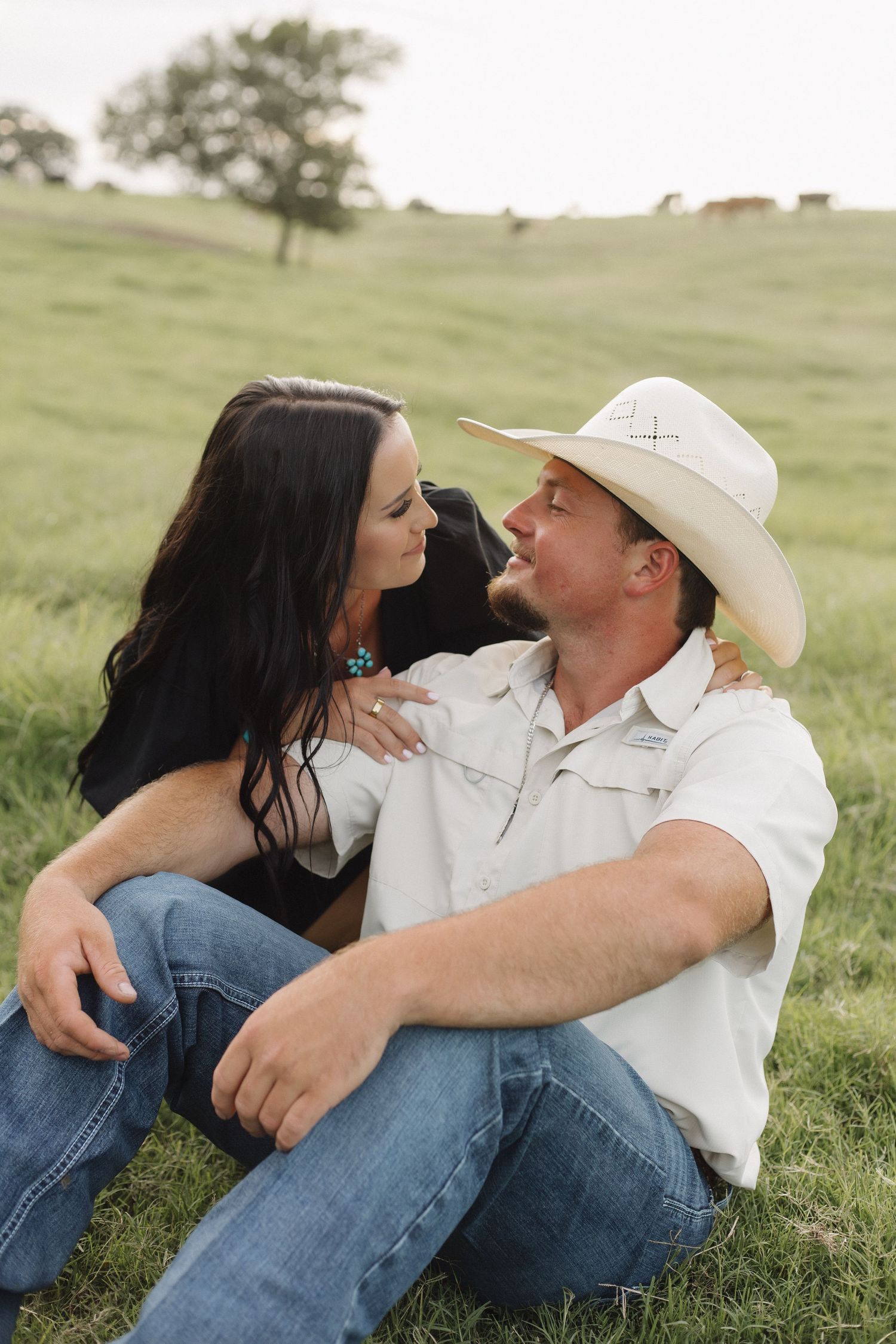 Couple in western attire sharing intimate moment on grassy hillside.