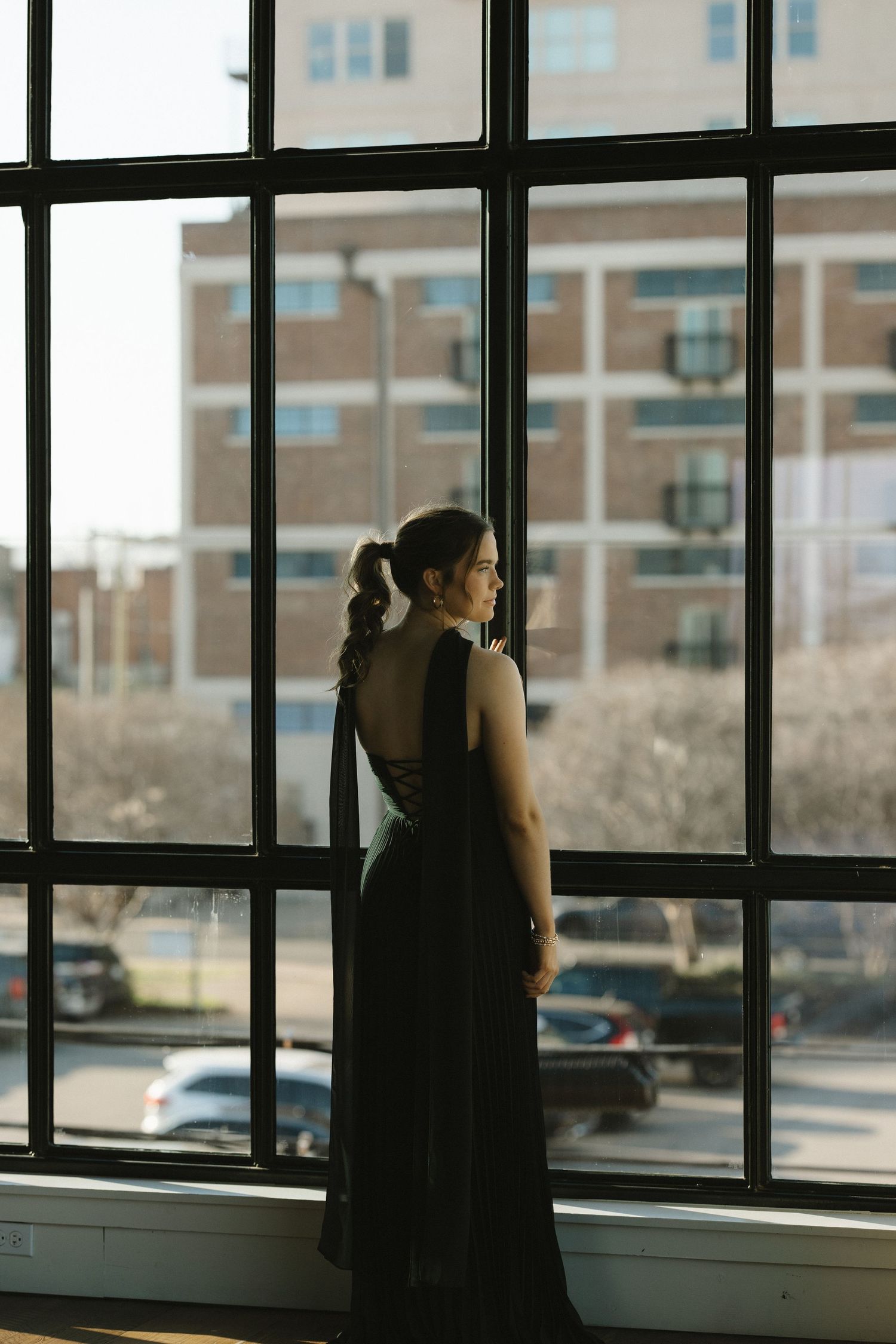 A silhouetted figure stands by large industrial windows in a modern building interior with natural light streaming in.