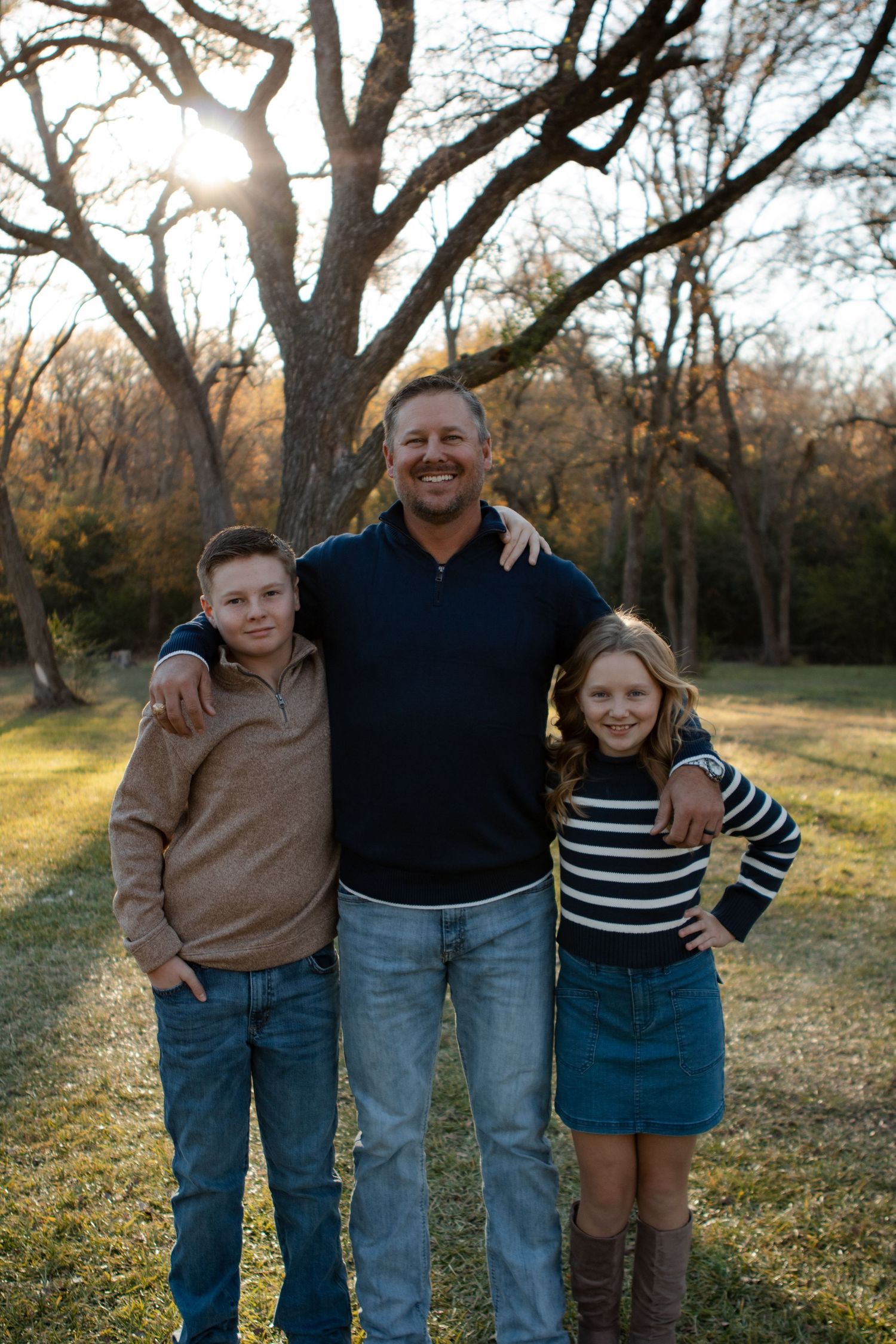 Father and children pose together on grassy hill during golden hour photo session.