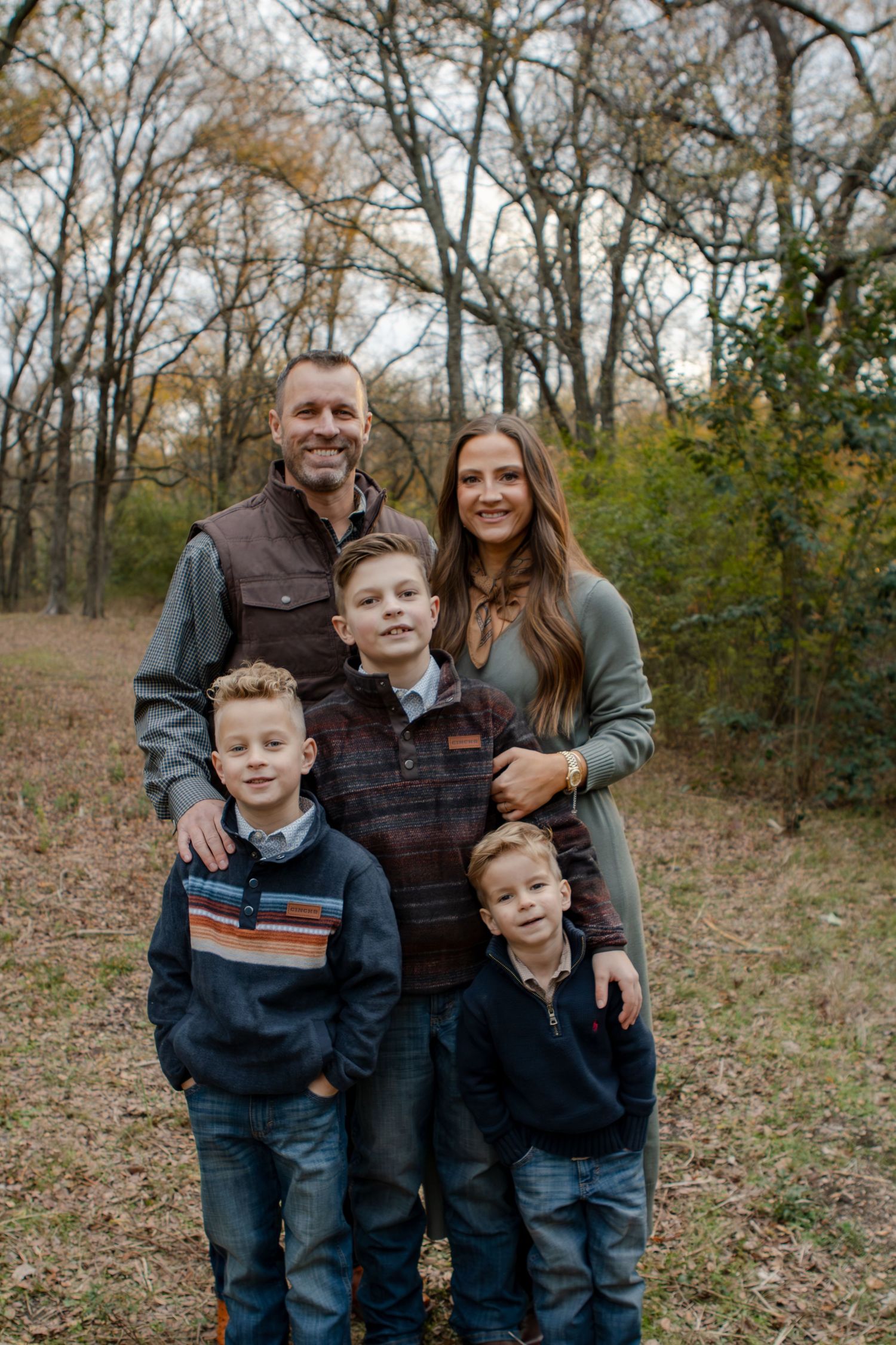 Happy family with three children pose together for outdoor portrait in wooded setting.