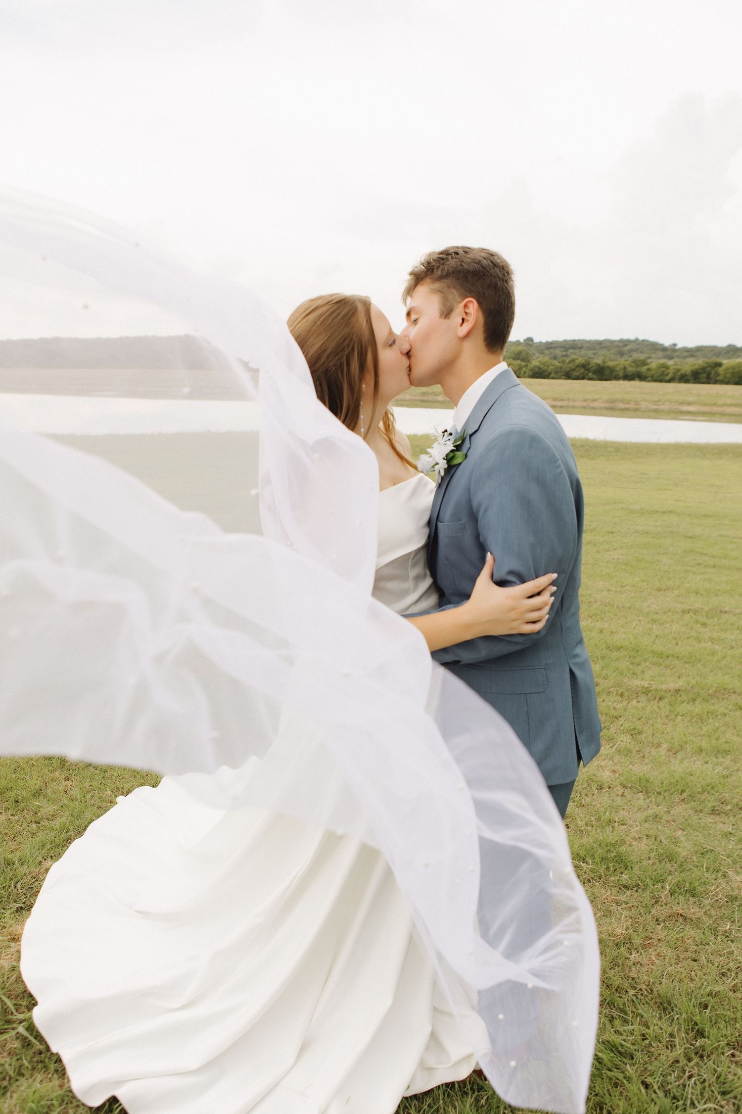 Wedding couple embracing in a field with bride's veil flowing in the wind.