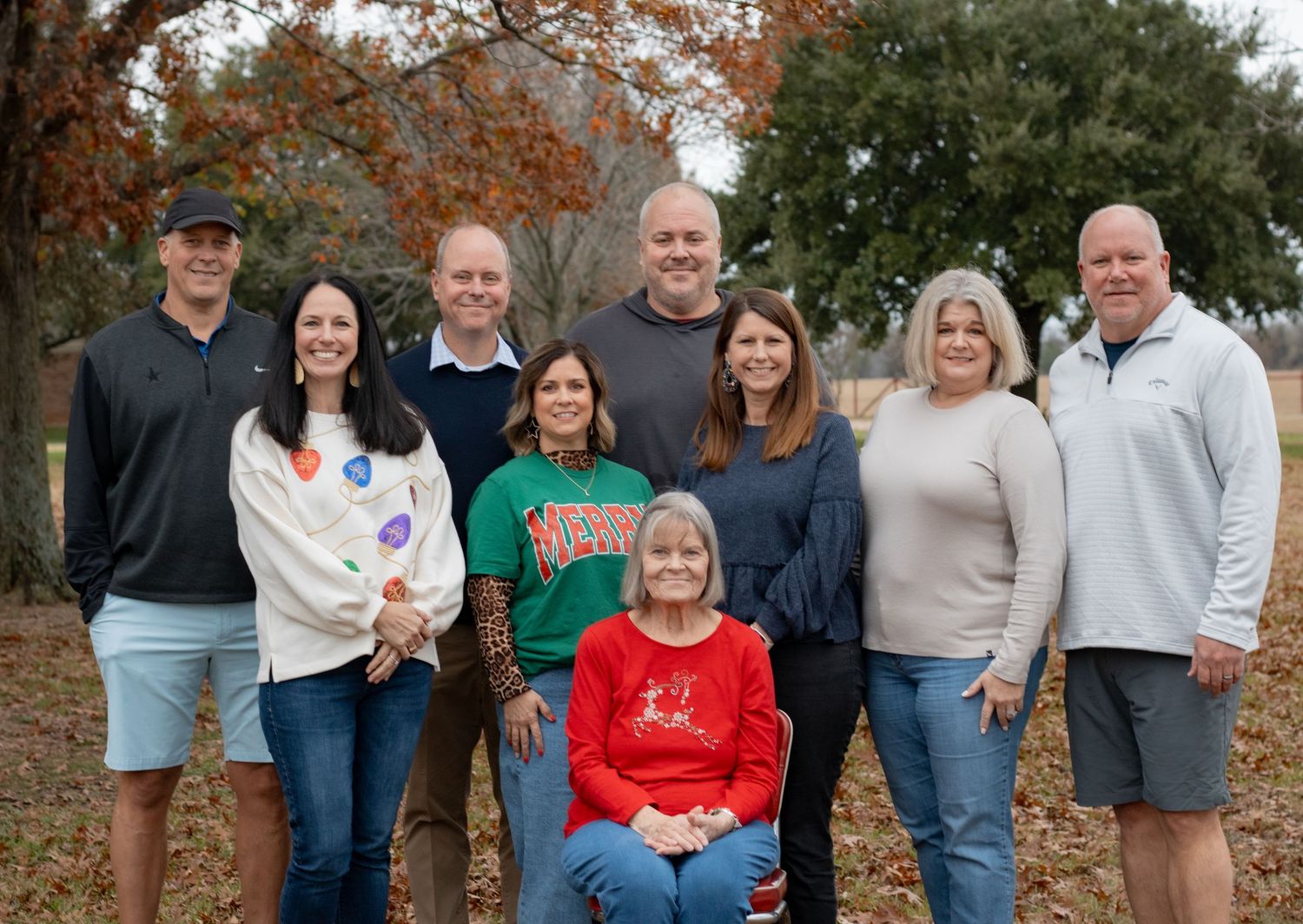 Extended family gathering outdoors for group photos during autumn with fall foliage in background.