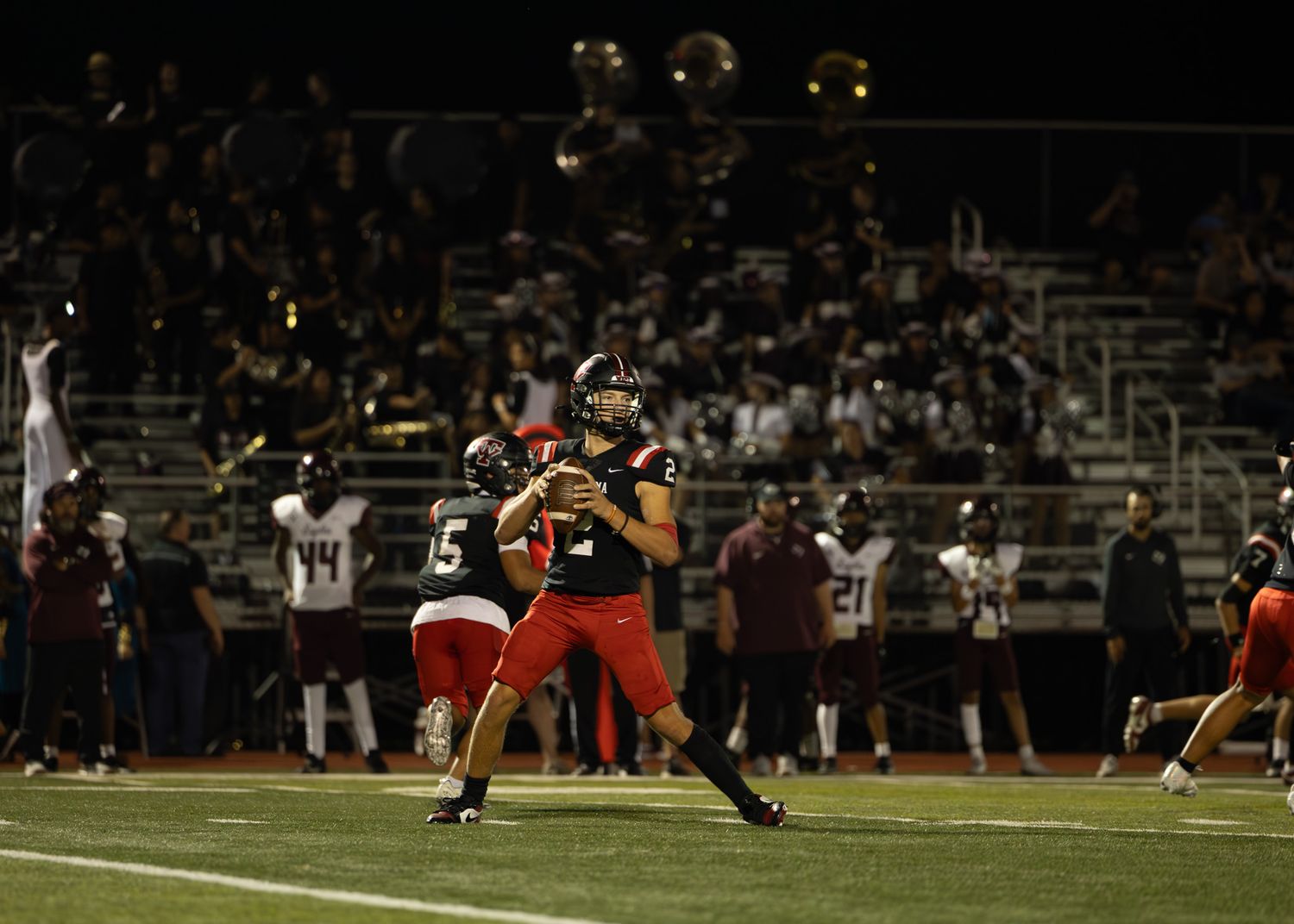 Night football game action with players in red and black uniforms.