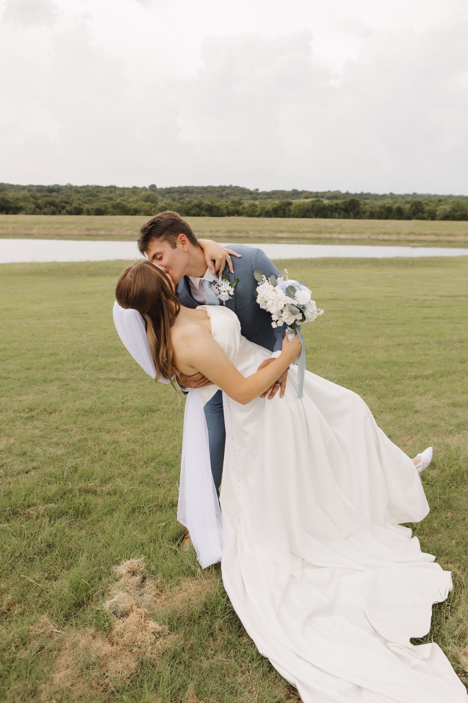 Newlyweds share romantic dance pose in an open field with flowing white wedding dress.