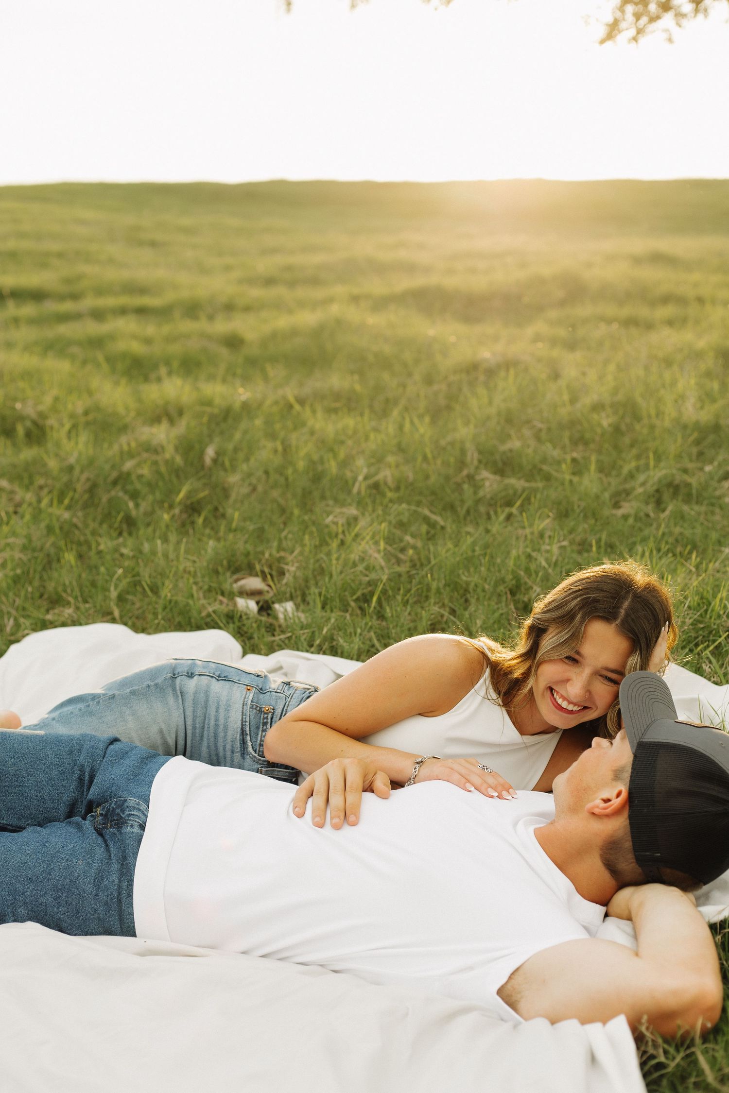 A couple lying together on grass during golden hour in a romantic outdoor photo session.