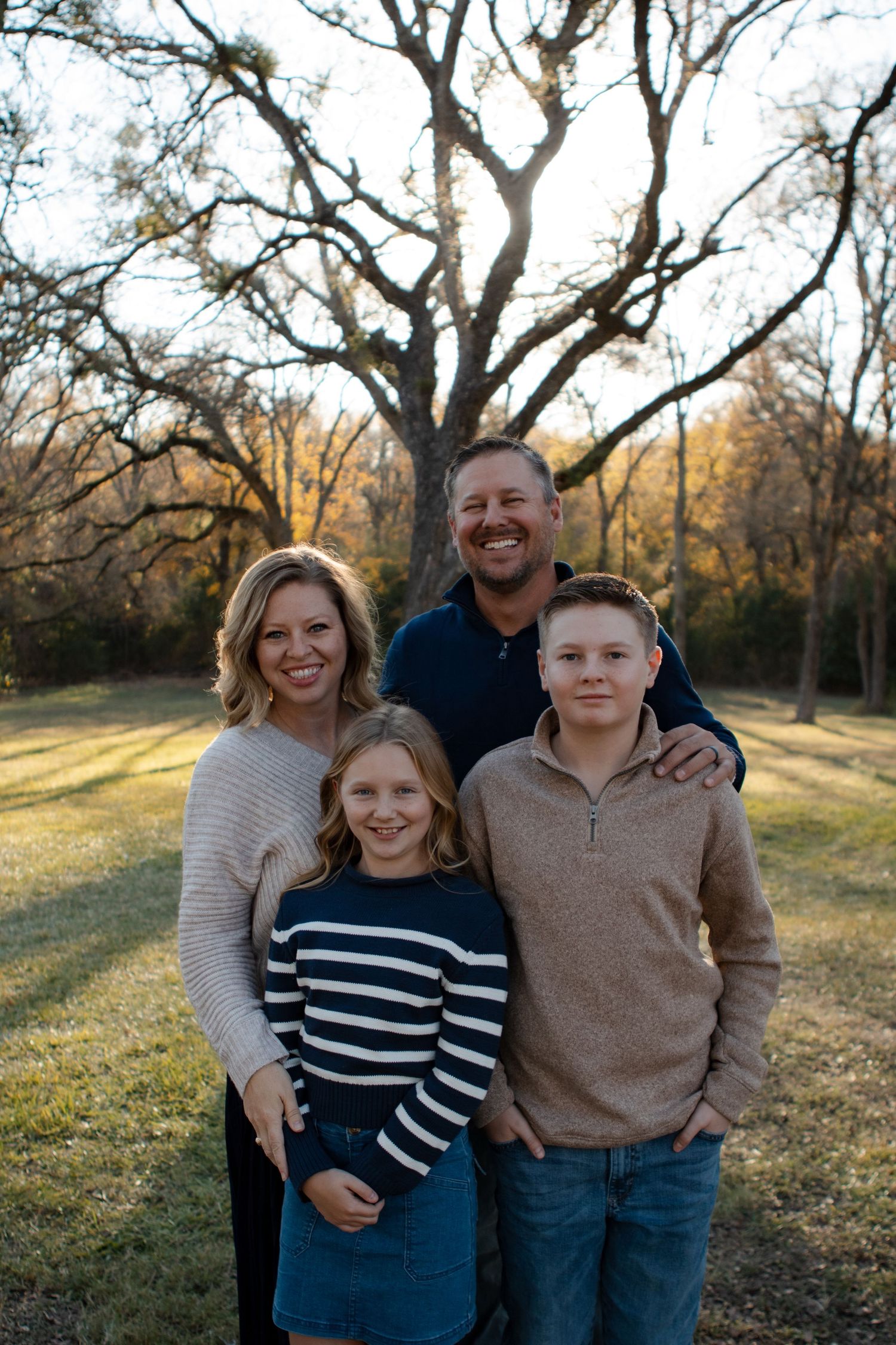 Family portrait session in a park during golden hour with trees in background.