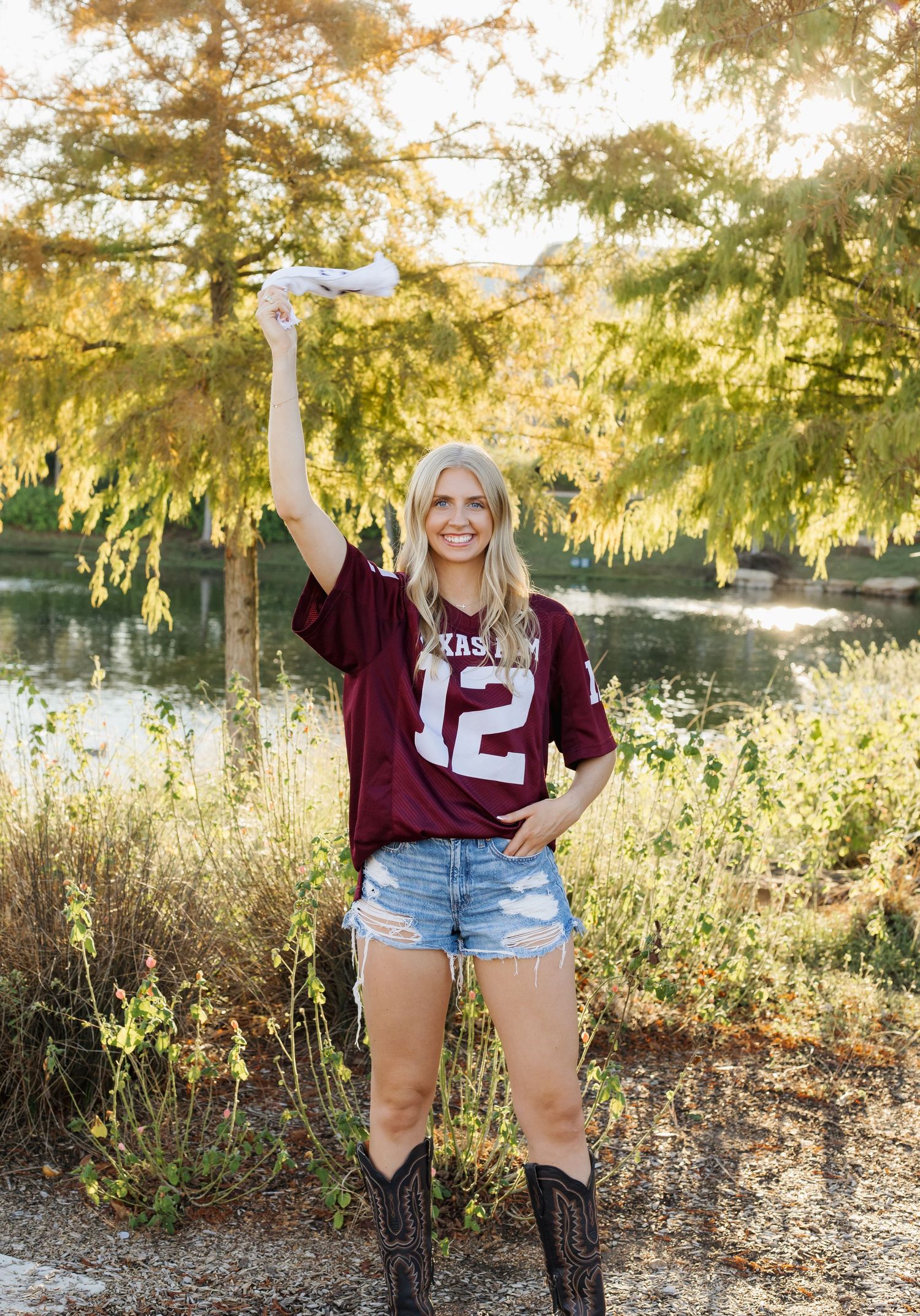 Woman in maroon jersey and denim shorts posing in outdoor setting with golden sunlight.