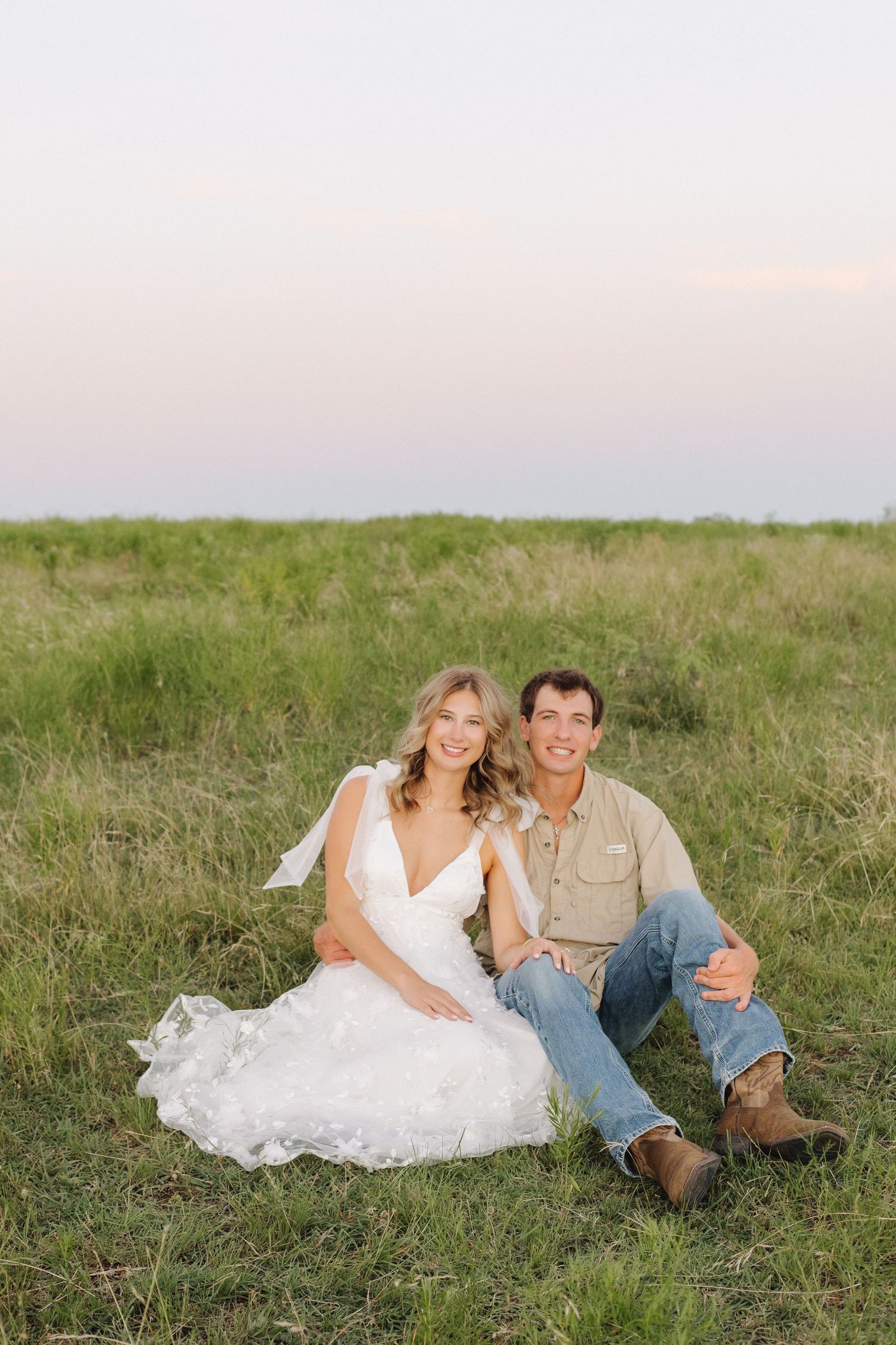 Couple relaxing together on grassy hillside during golden hour.
