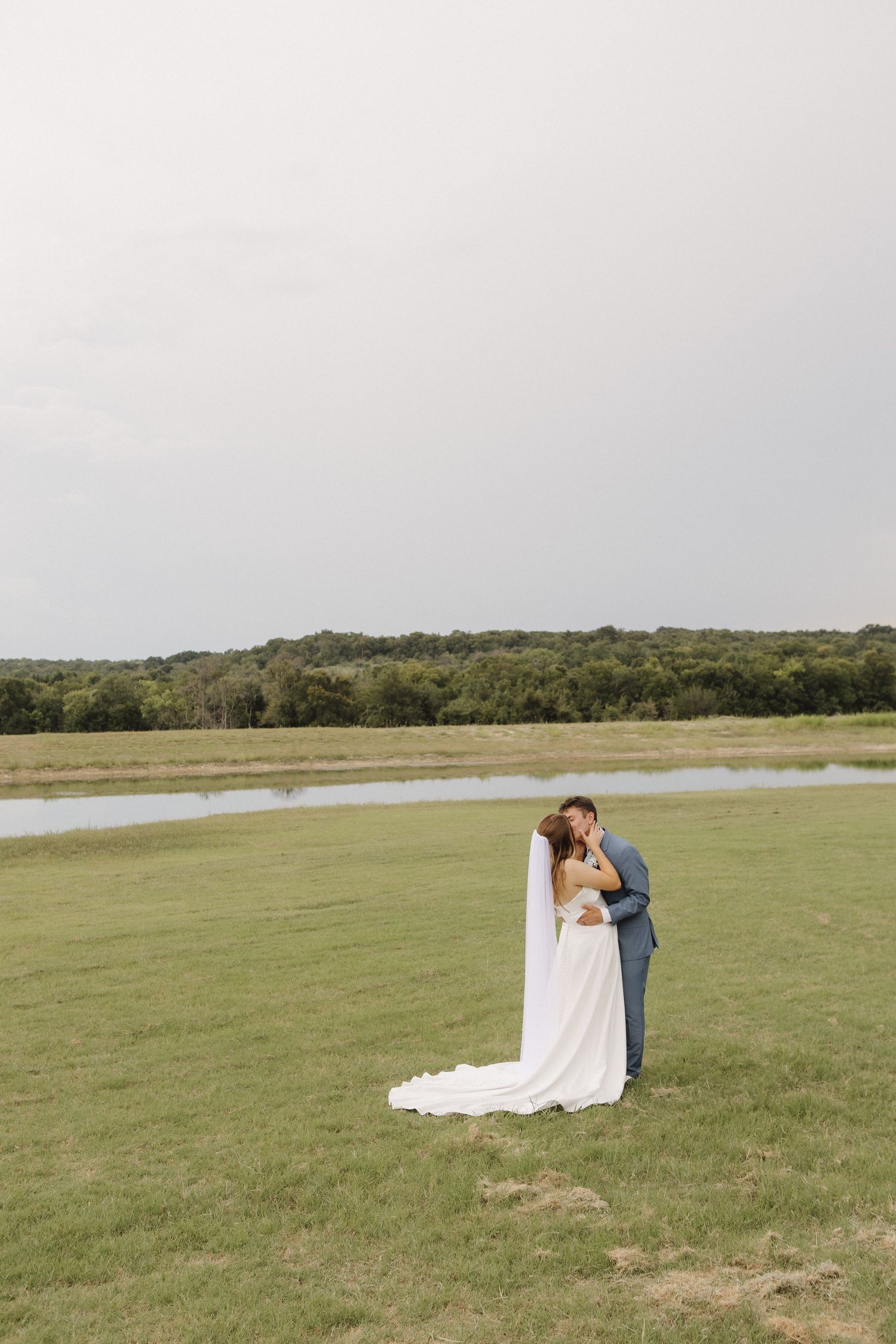 Romantic wedding couple sharing an intimate moment in an open field with scenic landscape.