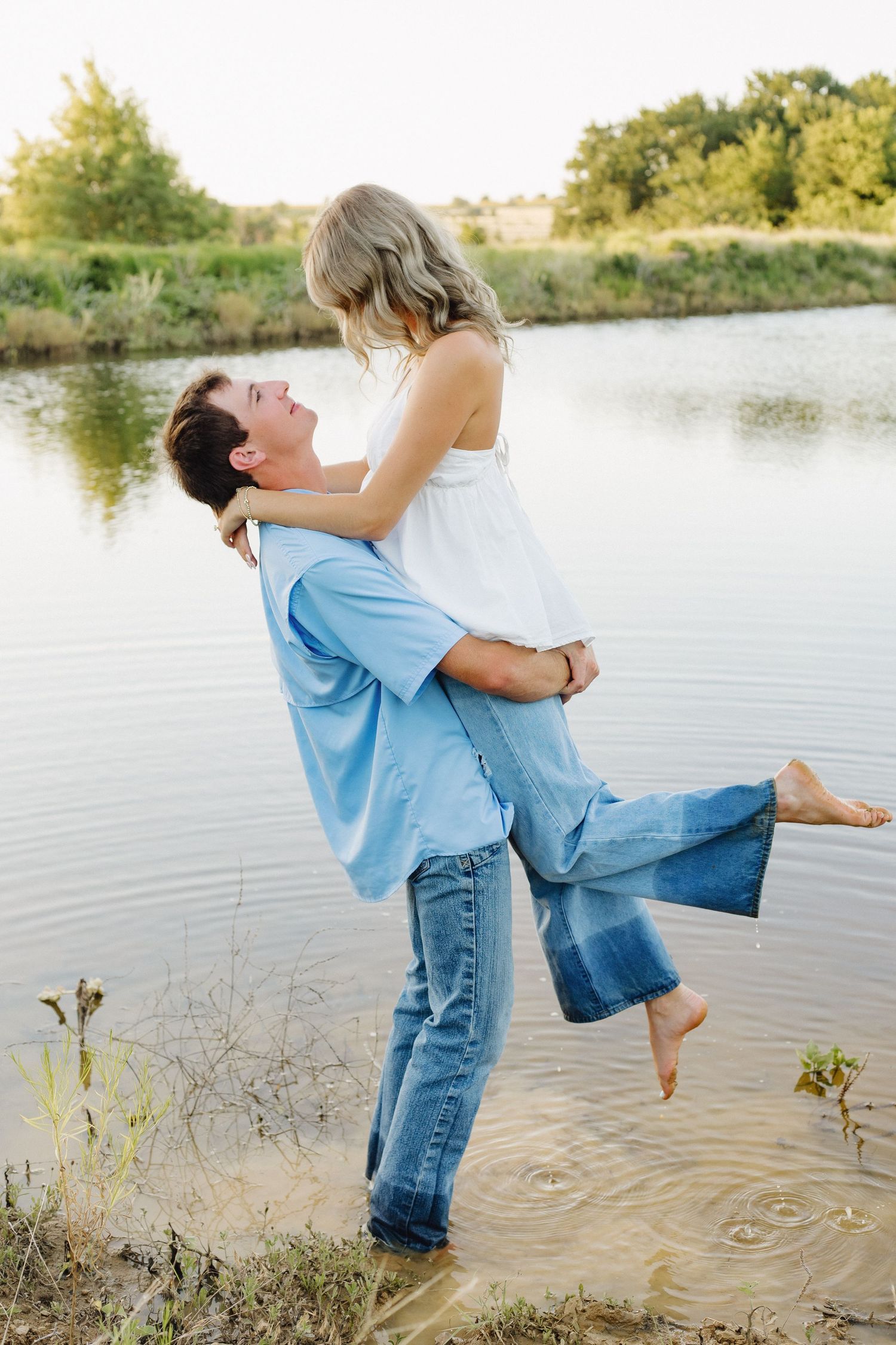 Romantic couple playing in shallow water at sunset by a lake.