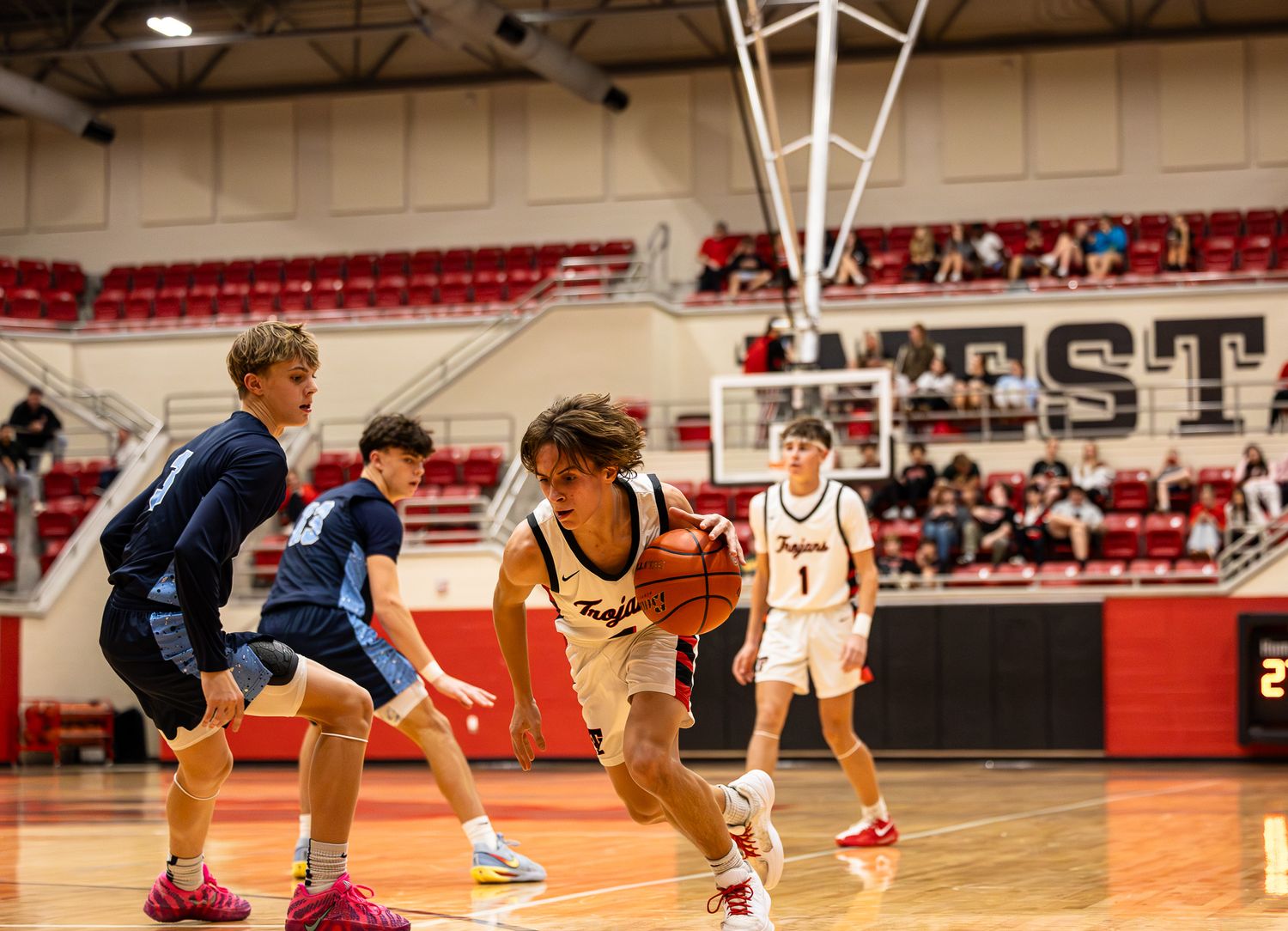 Basketball players competing in an indoor gymnasium with red bleachers.