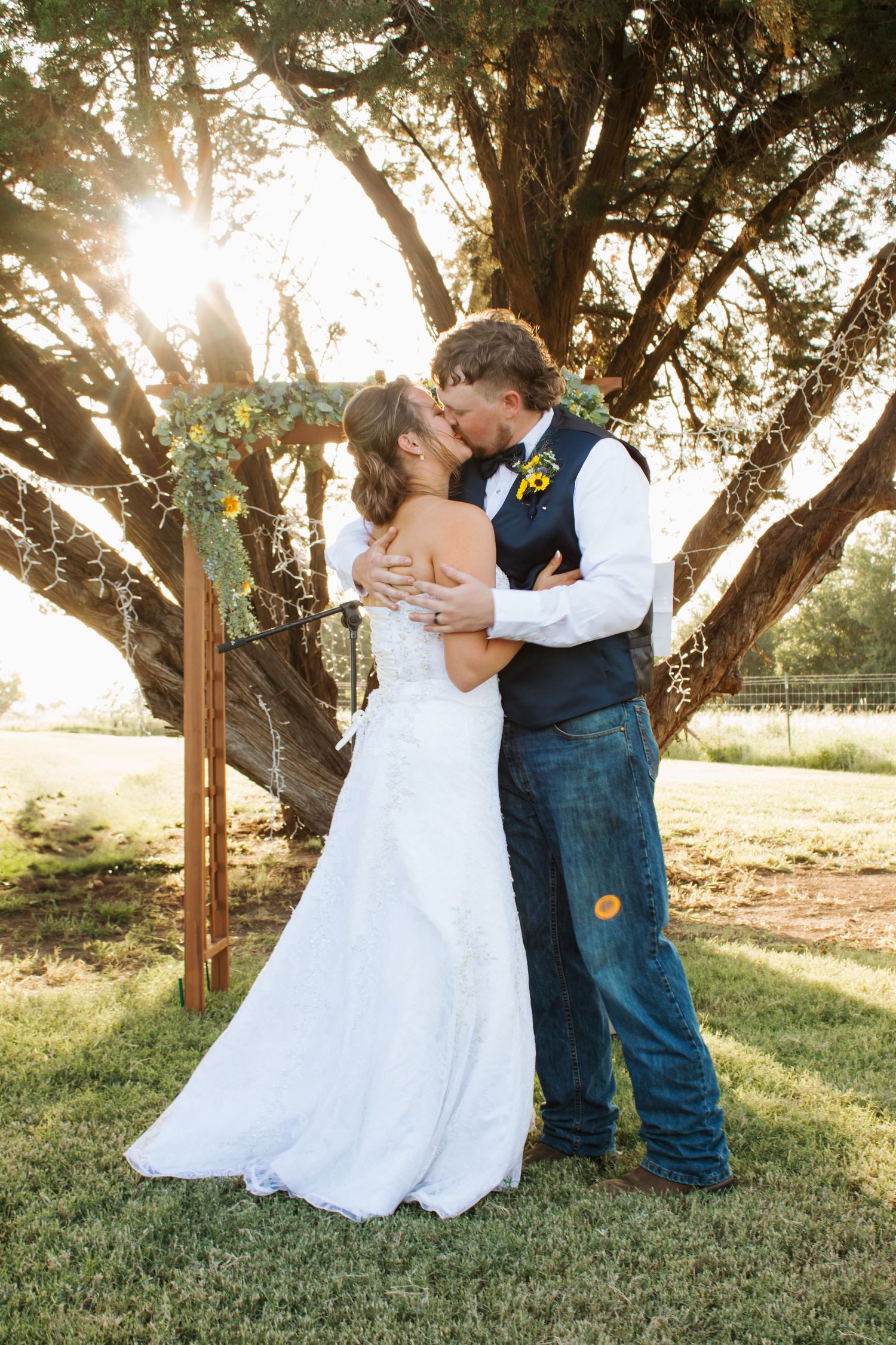 Newlyweds share romantic kisses under trees at sunset in rustic outdoor wedding setting.