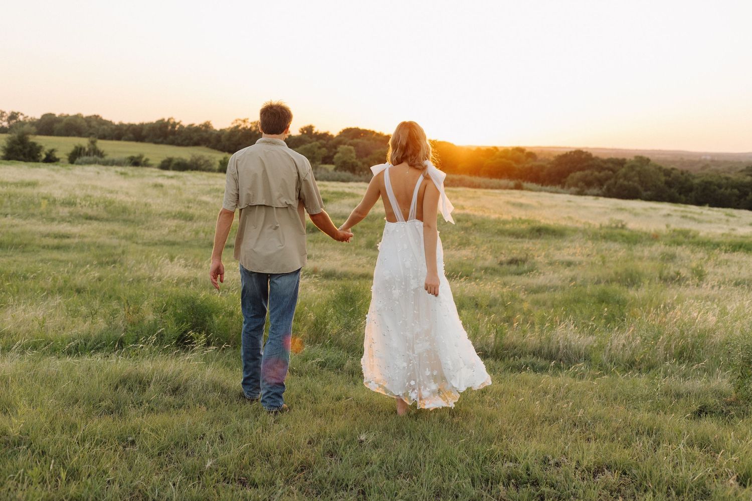 Couple walking hand in hand through a golden field at sunset.
