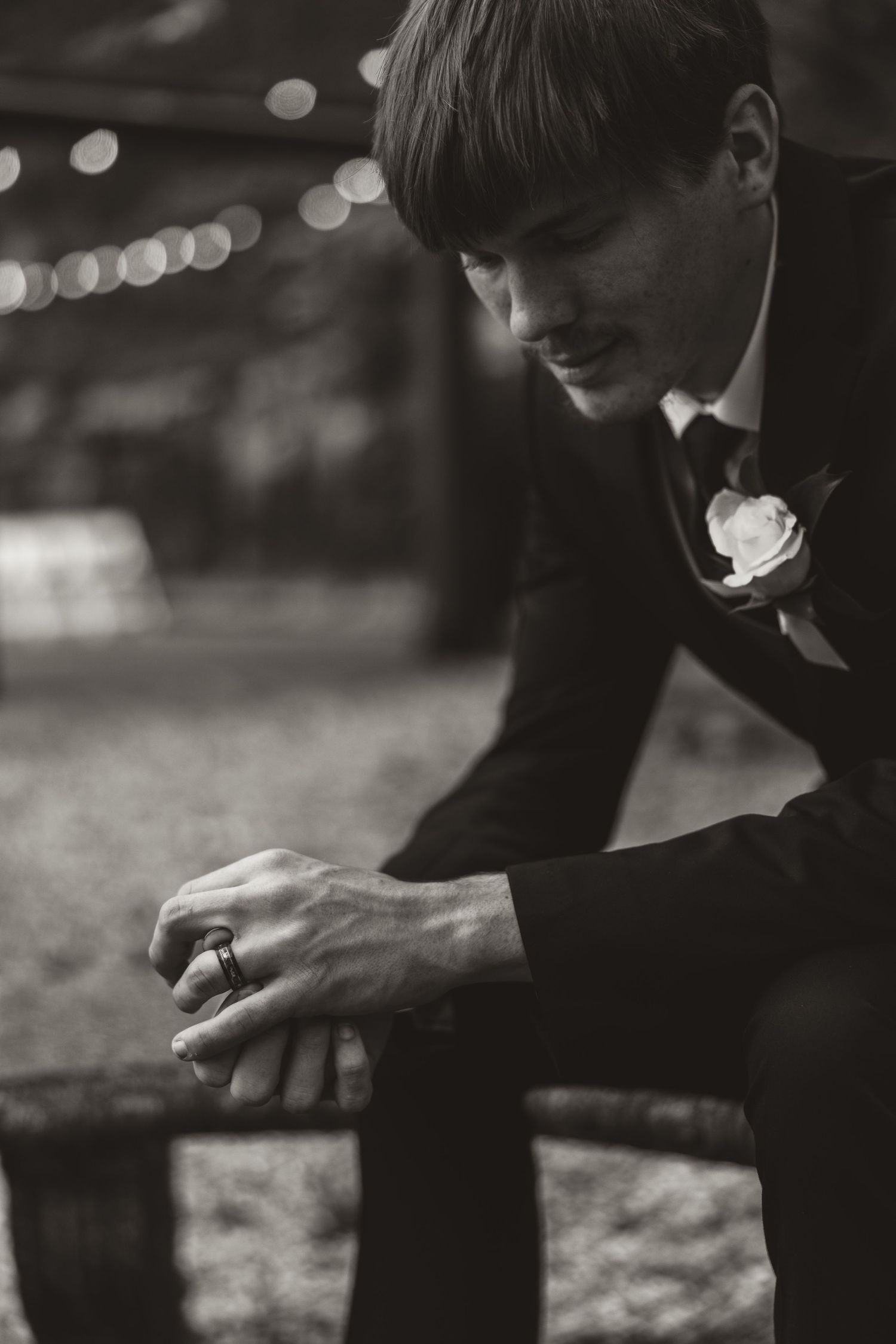 A person in dark clothing sits on the ground examining something in their hands while surrounded by blurred bokeh lights.