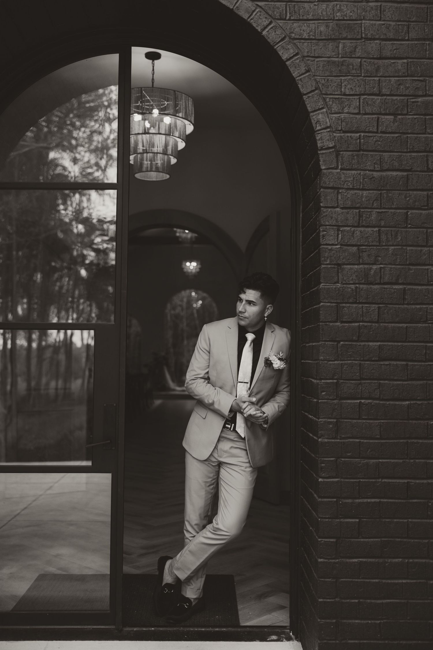 Man in light suit leaning against brick archway in classic black and white portrait.