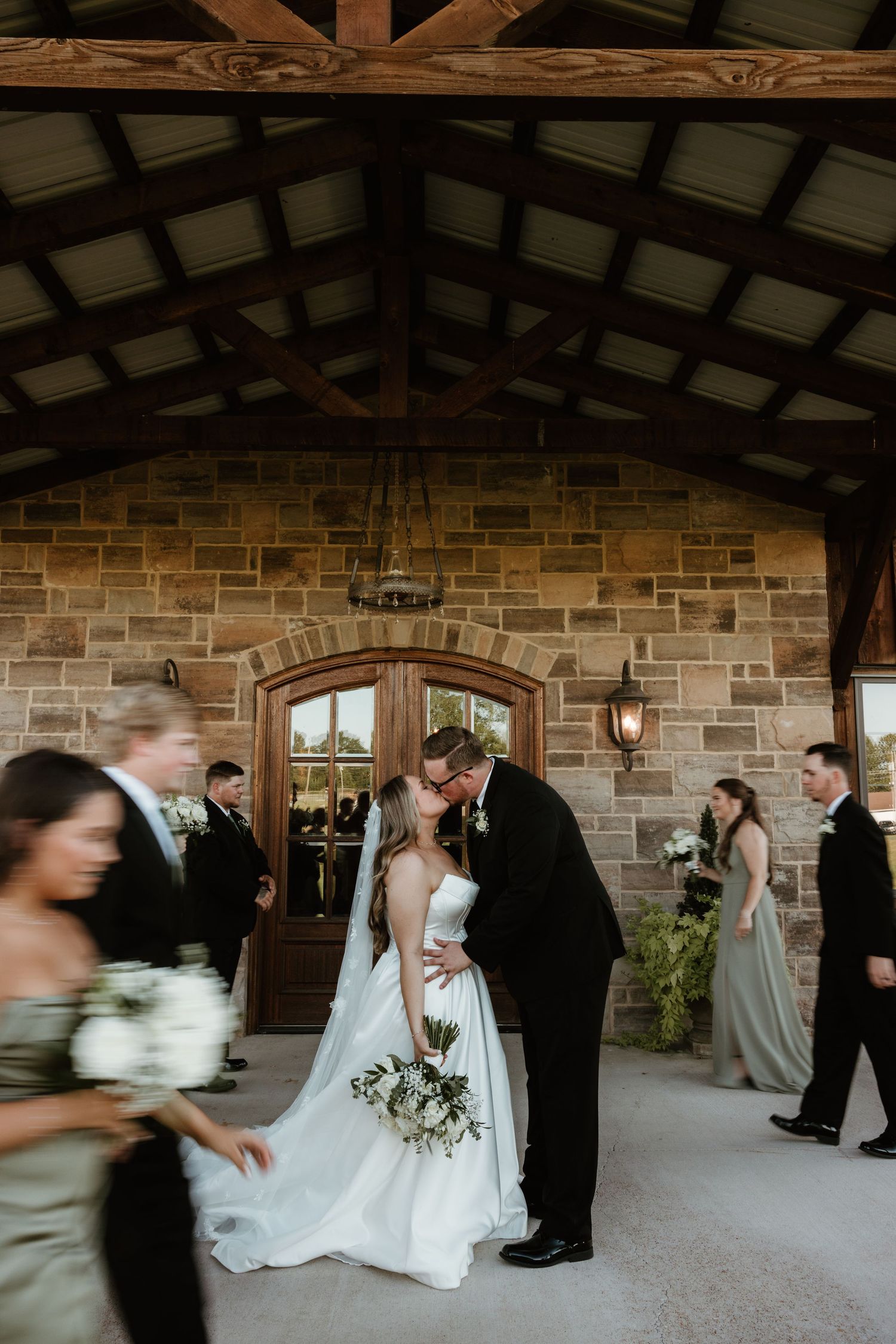 Wedding celebration outside a rustic stone venue with exposed wooden beams and lantern lighting.
