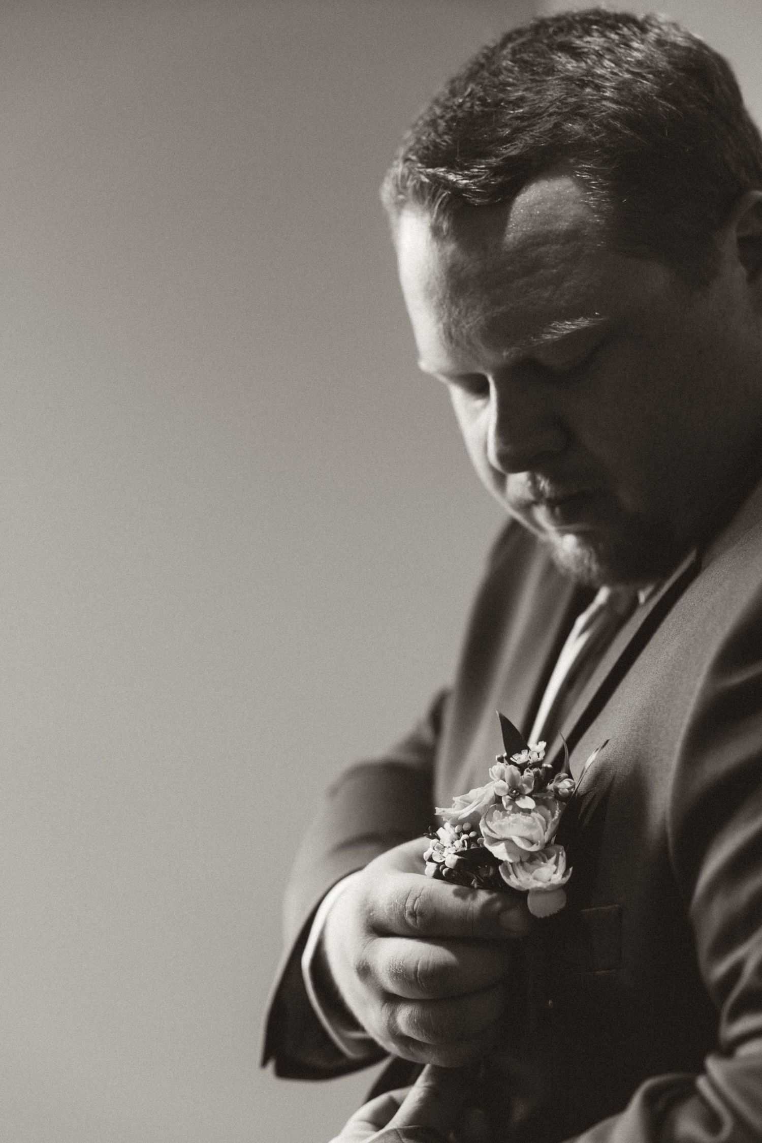 A black and white photo of someone in formal attire adjusting their boutonniere during a wedding ceremony.