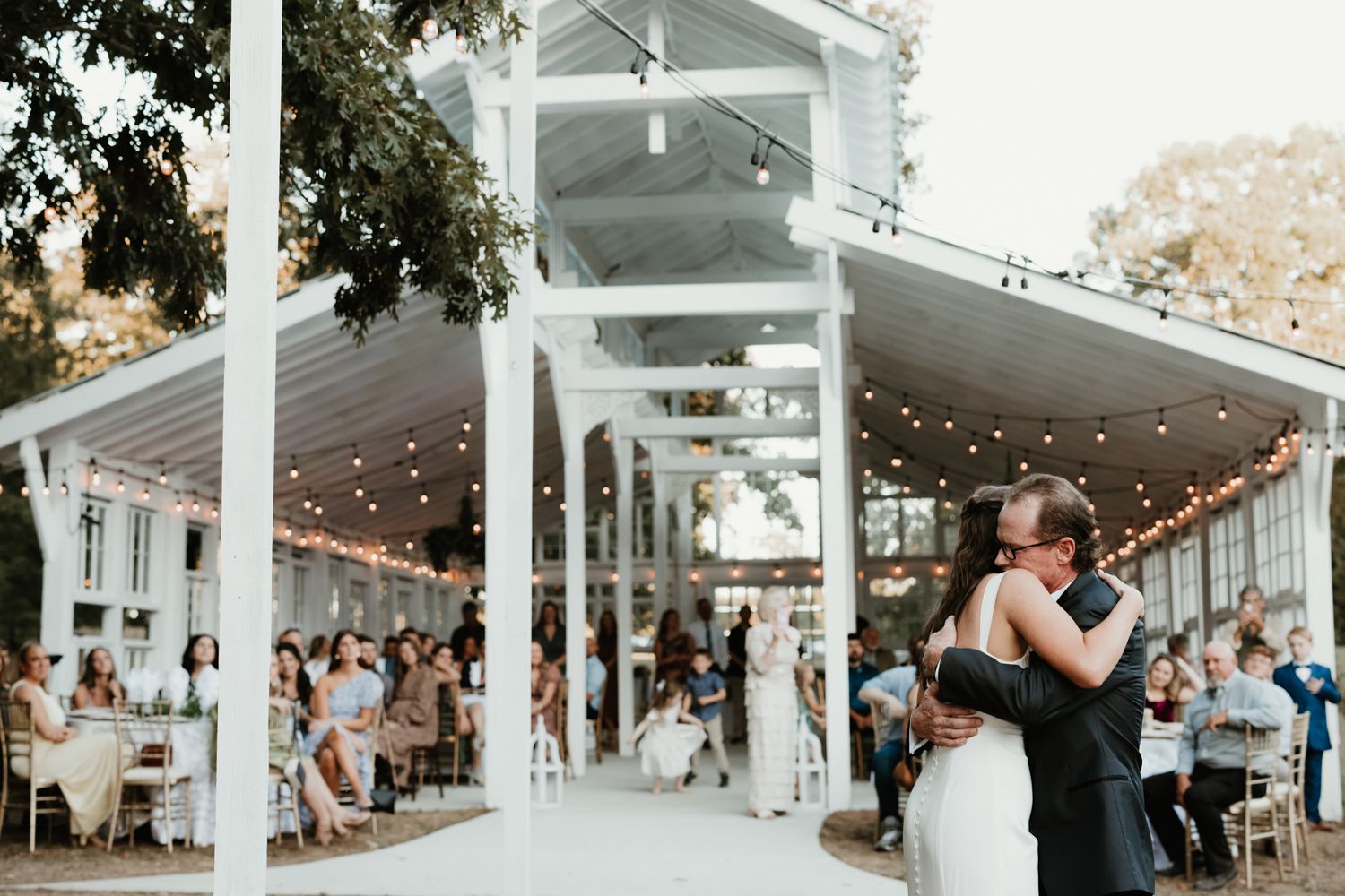 White wedding venue with string lights and guests celebrating during a reception.